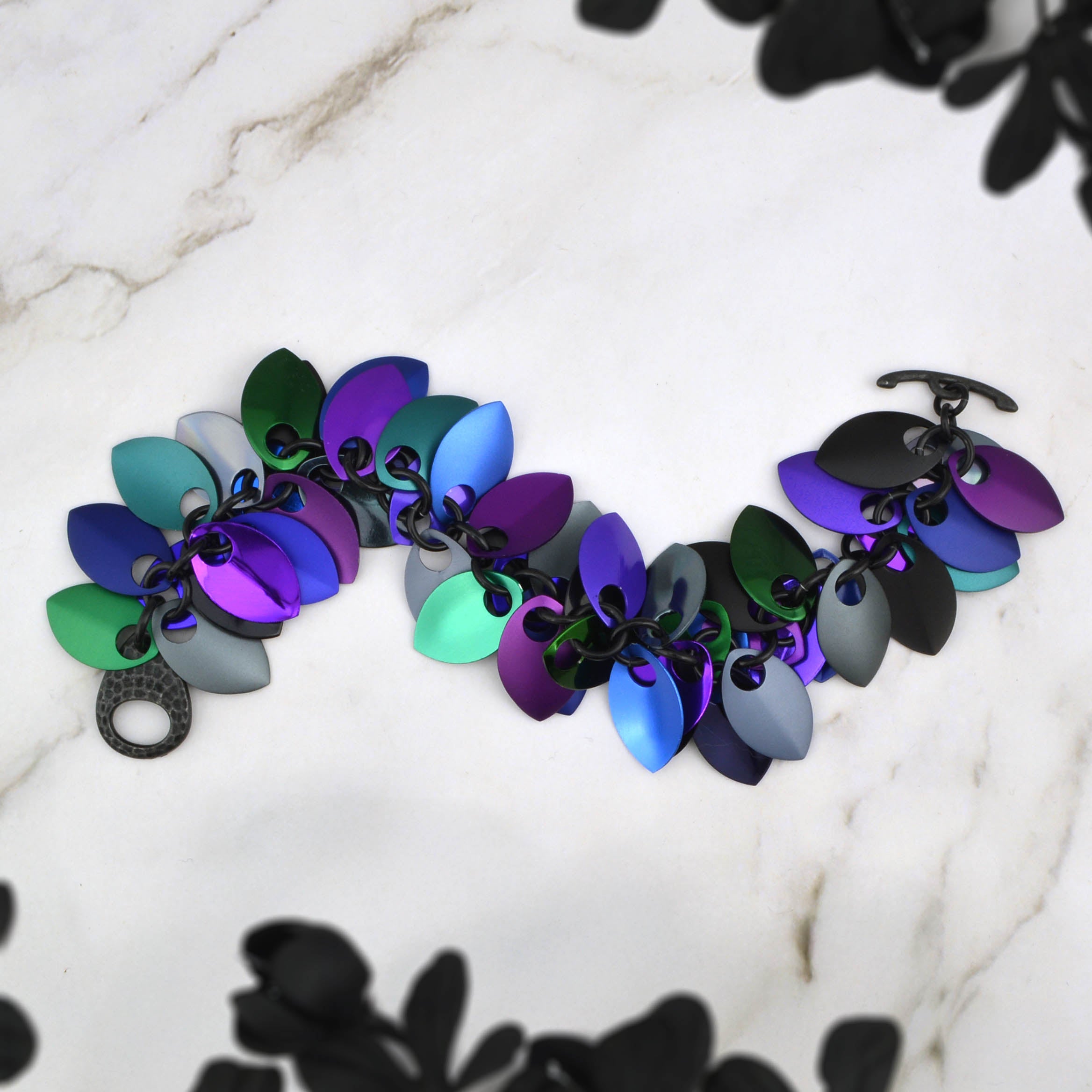 Aerial view of the full length of the Dark Mermaid cascading scalemaille bracelet lying in an S-curve, clearly showing the colors and lead-free pewter toggle clasp detail.