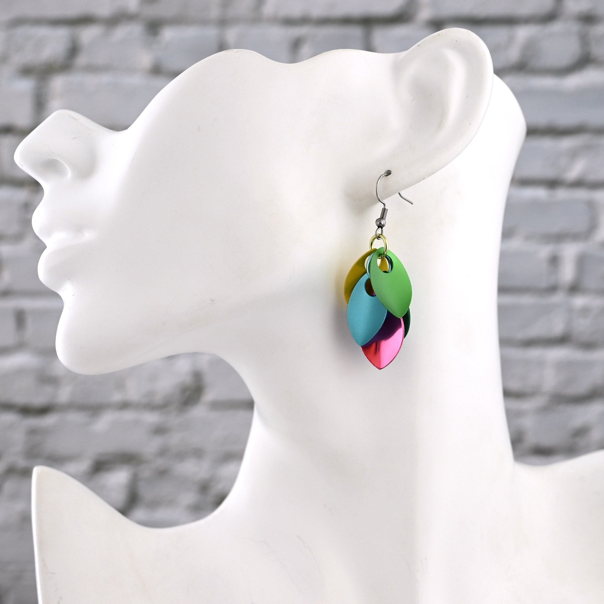 Side view of a white mannequin wearing the Blossom Short Cascading Leaves dangles, showing how the 2-inch drop sits elegantly just below the earlobe. The scalemaille earrings feature saturated pastels in pink, yellow, green and blue.