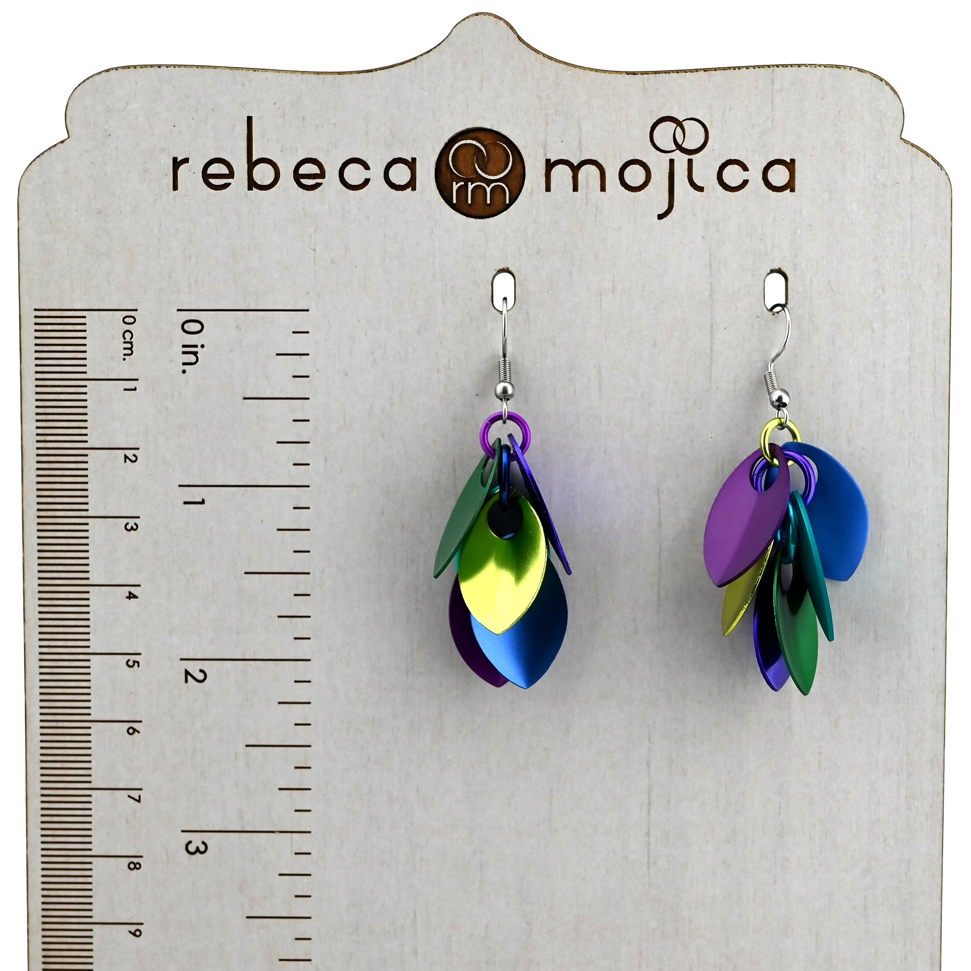Peacock Cascading Earrings displayed on a Rebeca Mojica branded display with a ruler, showing a length of approximately 2.25 inches.
