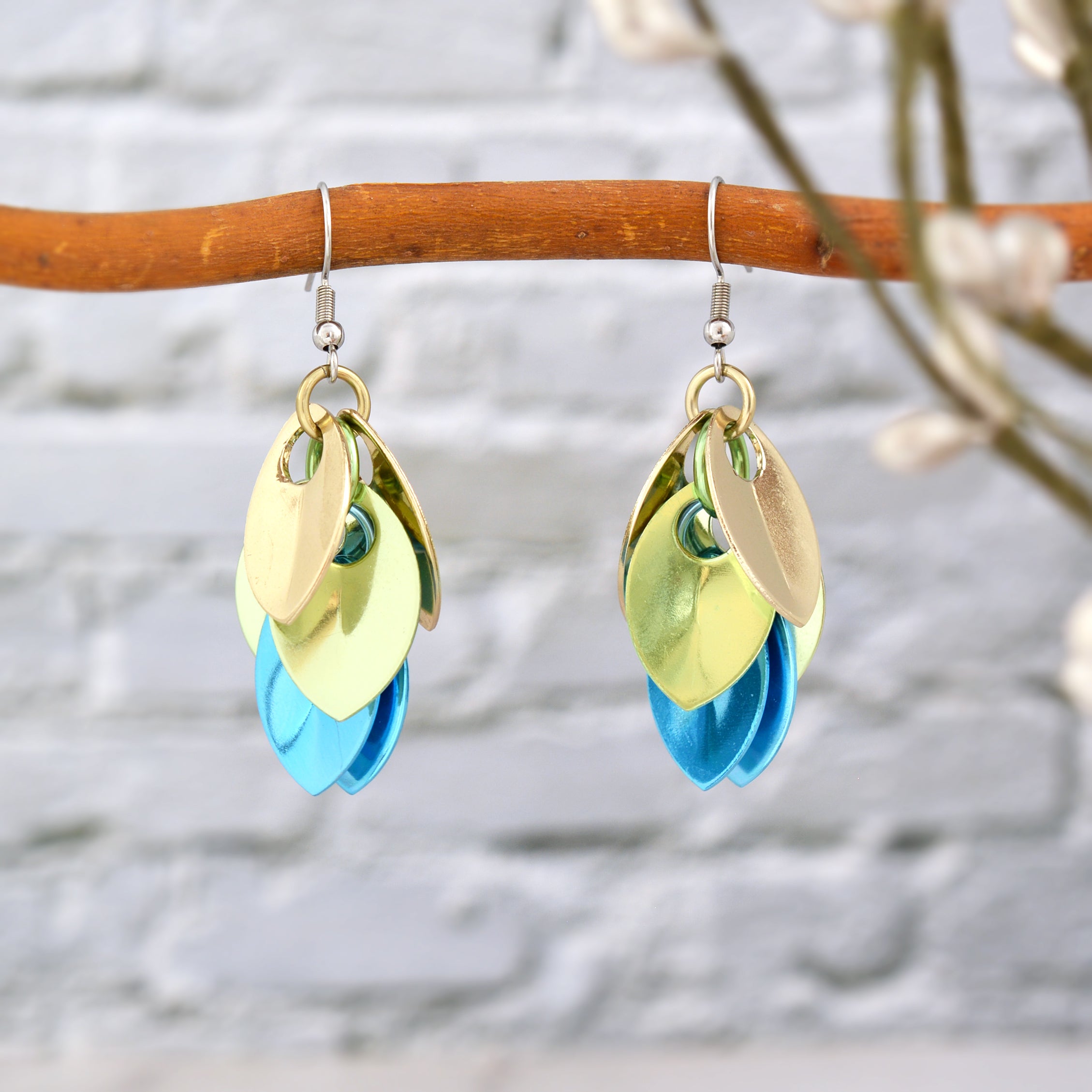 Close-up of seashell ombre chainmaille earrings hanging on a tree branch, highlighting the champagne, seafoam, and light blue colors.