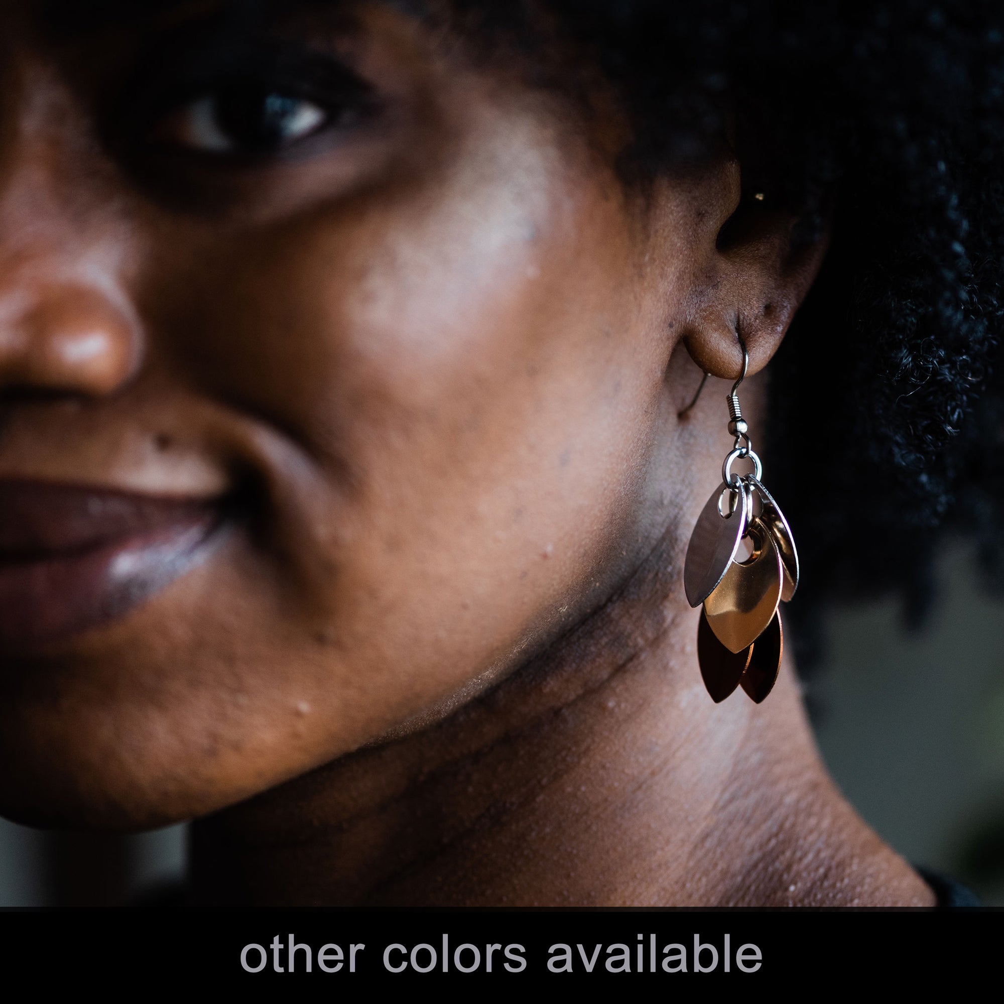 Close-up of a Black woman modeling the Short Cascading Leaves chainmaile earrings in another colorway (silver/beige) with the text "other colors available."