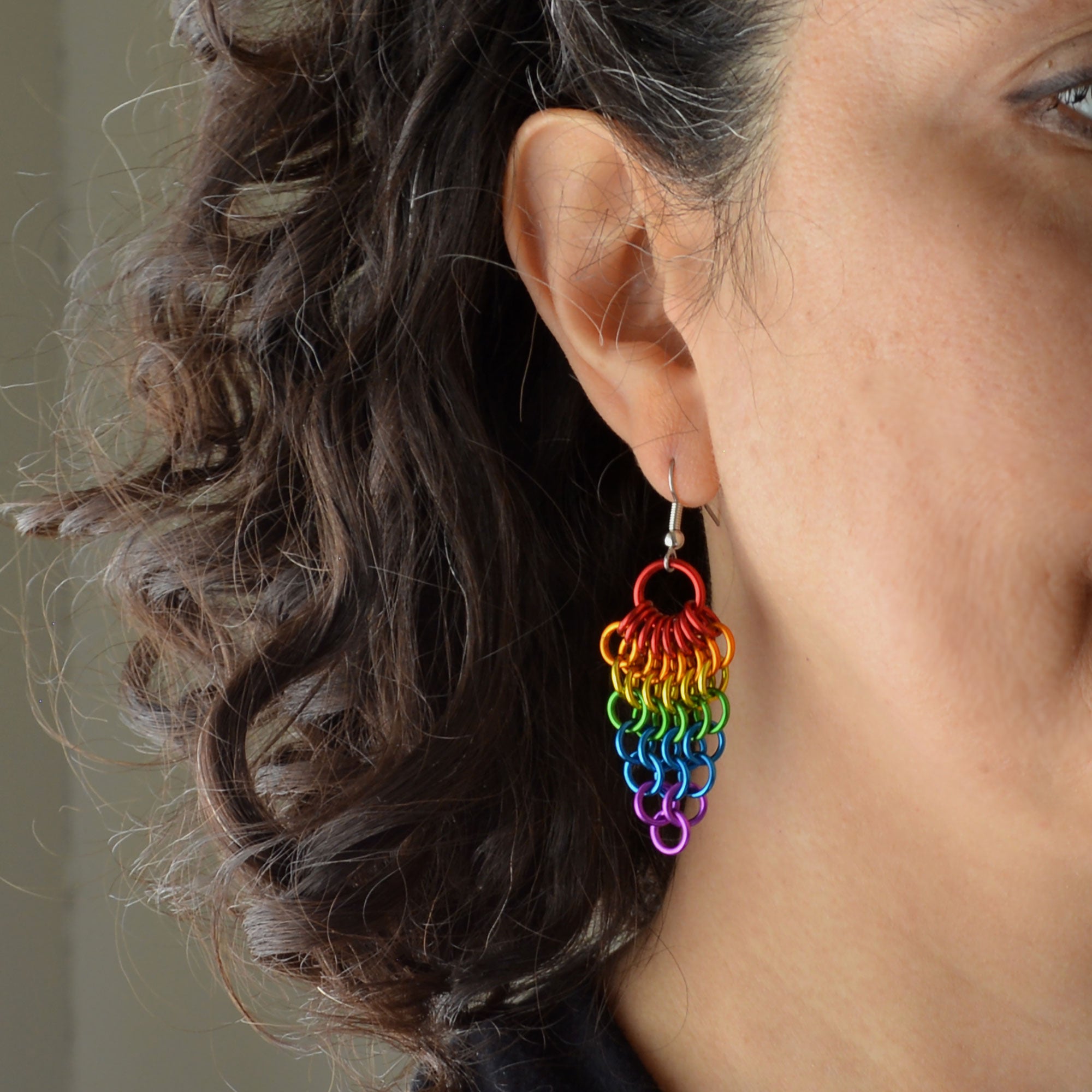 A close-up view of artisan Rebeca Mojica wearing a rainbow Mesh Cluster earring, showing the intricate details and how it looks on her ear.