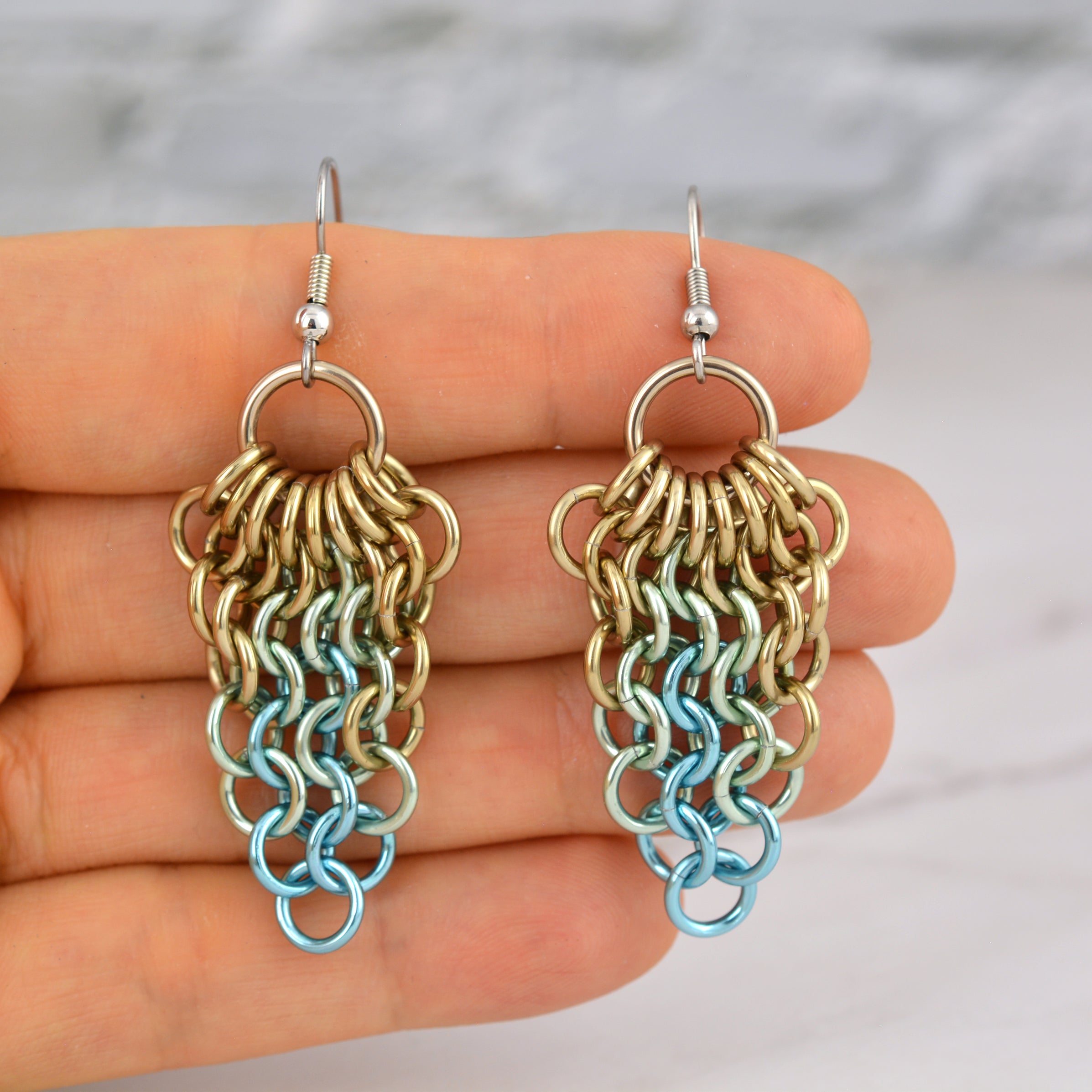 Closeup of chainmaille cluster mesh earrings resting in the fingertips of chainmaille artisan Rebeca Mojica. This photo provides a sense of the scale and lightness of the jewelry.
