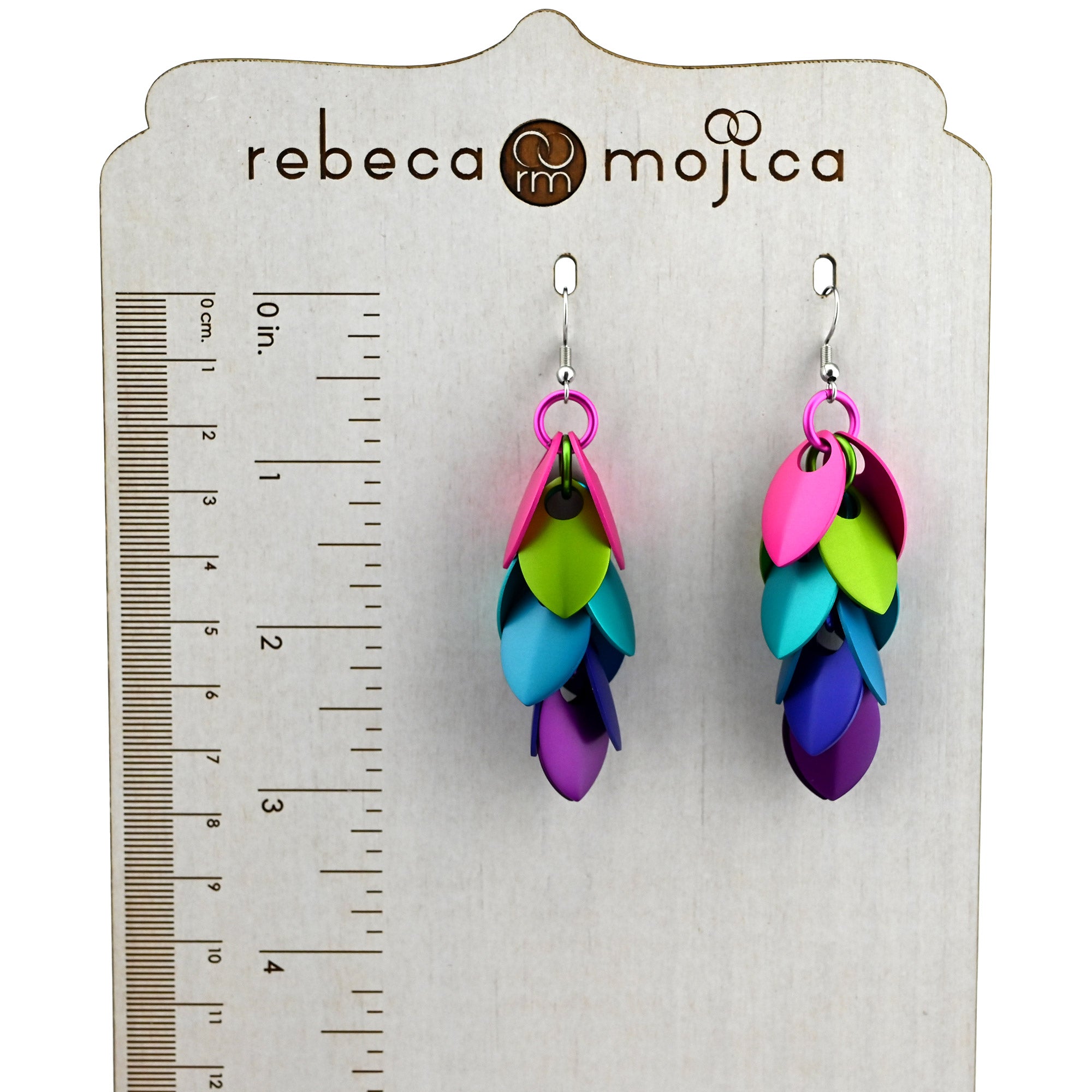 Electric Rainbow Long Feathered Earrings shown on a branded display stand with a ruler, measuring approximately 3 inches in length.
