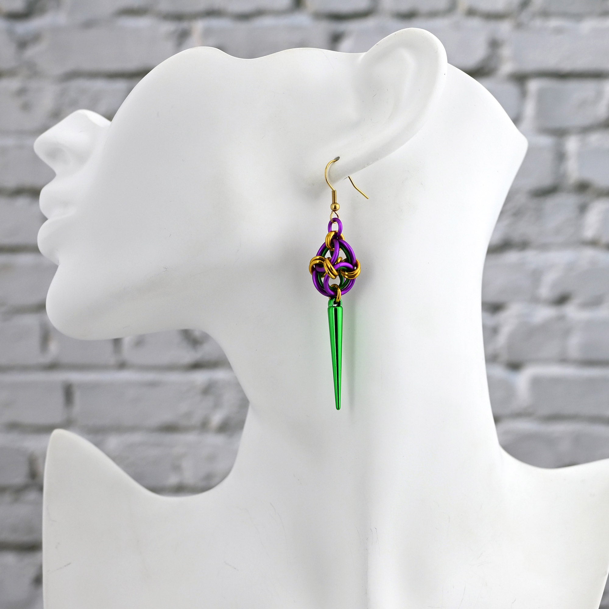 A side-view of a white mannequin bust wearing a single purple, gold, and green spiked polyhedron earring to show how it hangs and sits against the neck.