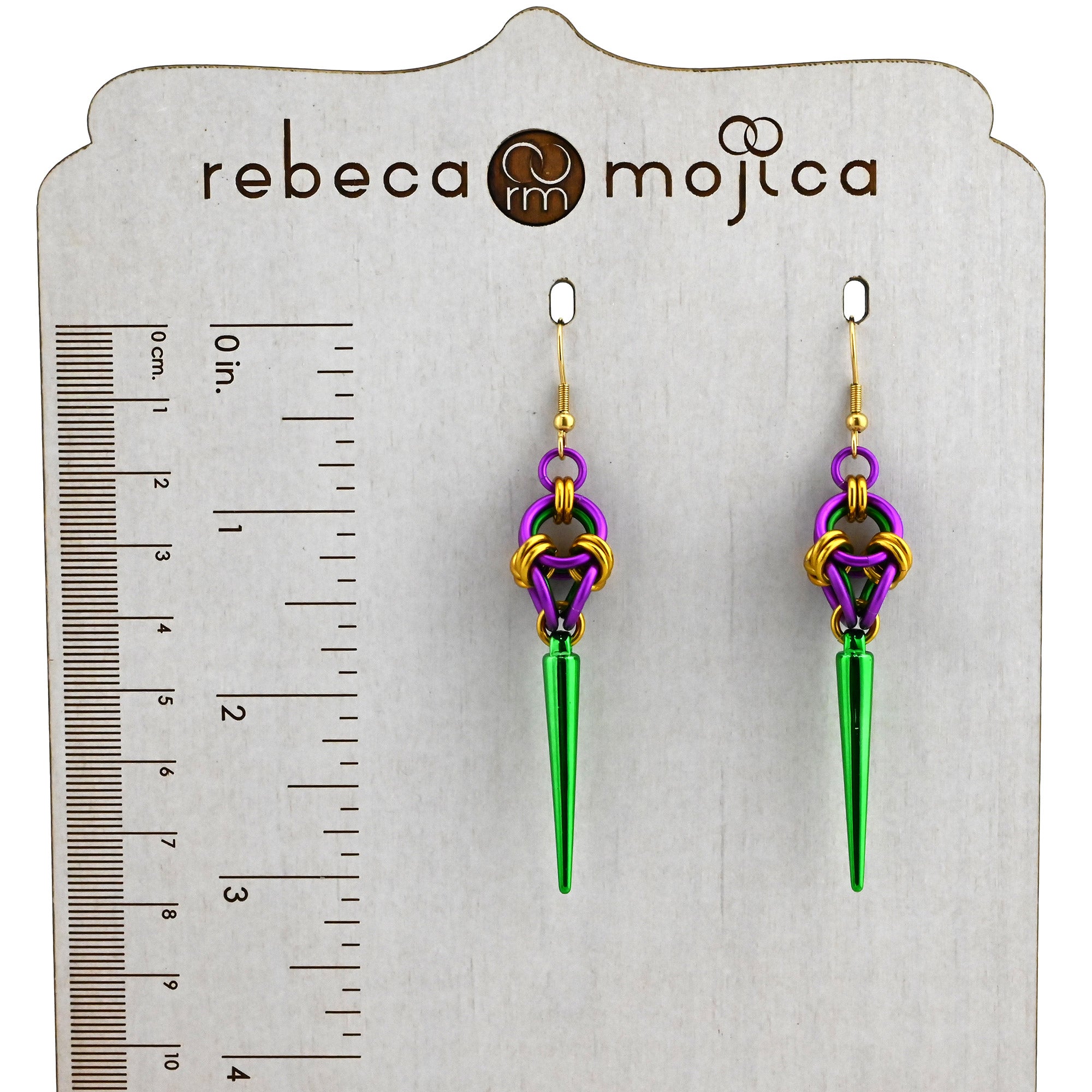 Mardi Gras spike earrings displayed on a Rebeca Mojica branded card next to a ruler showing a length of approximately 3 inches.