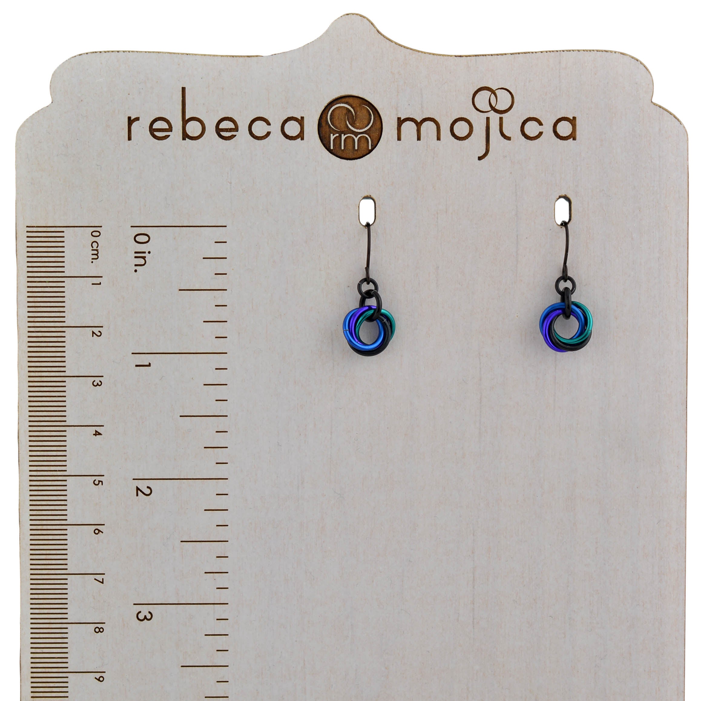Size reference for Rebeca Mojica's Mini Knot chainmaile earrings showing the 7/8-inch length on a branded wooden display with ruler.
