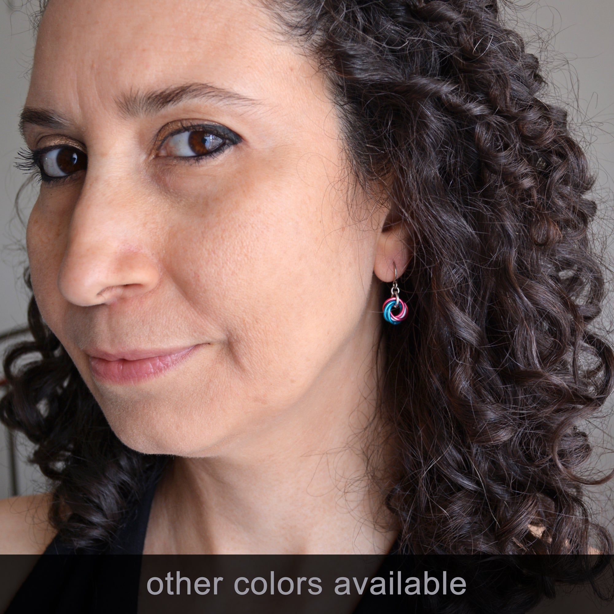 Artisan Rebeca Mojica modeling the tiny Mini Knot chainmaile earrings in an "other colors available" version (pink, blue, silver), for size and fit.