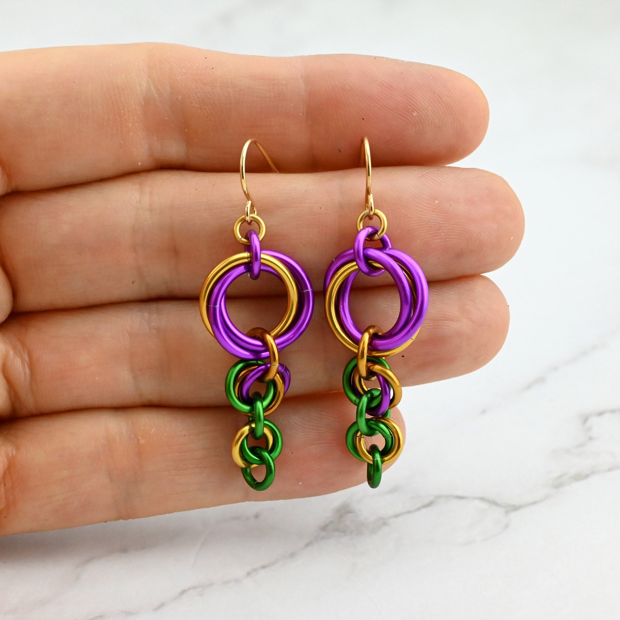 Mardi Gras ombre knot earrings held against fingertips to showcase the small, lightweight scale of the jewelry.