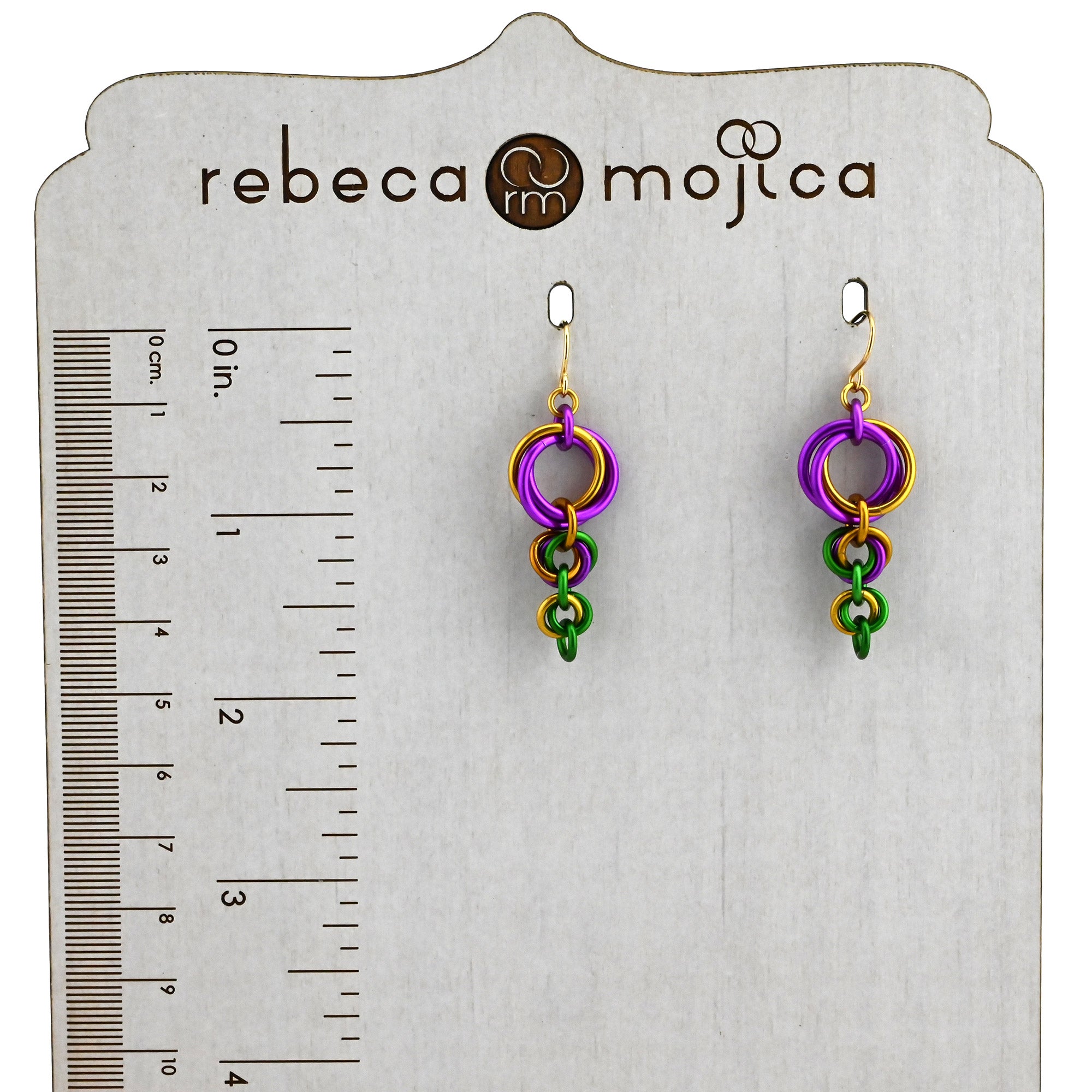 Kng Cake-inspired earrings on a Rebeca Mojica display card next to a ruler showing a length of about 1.75 inches.