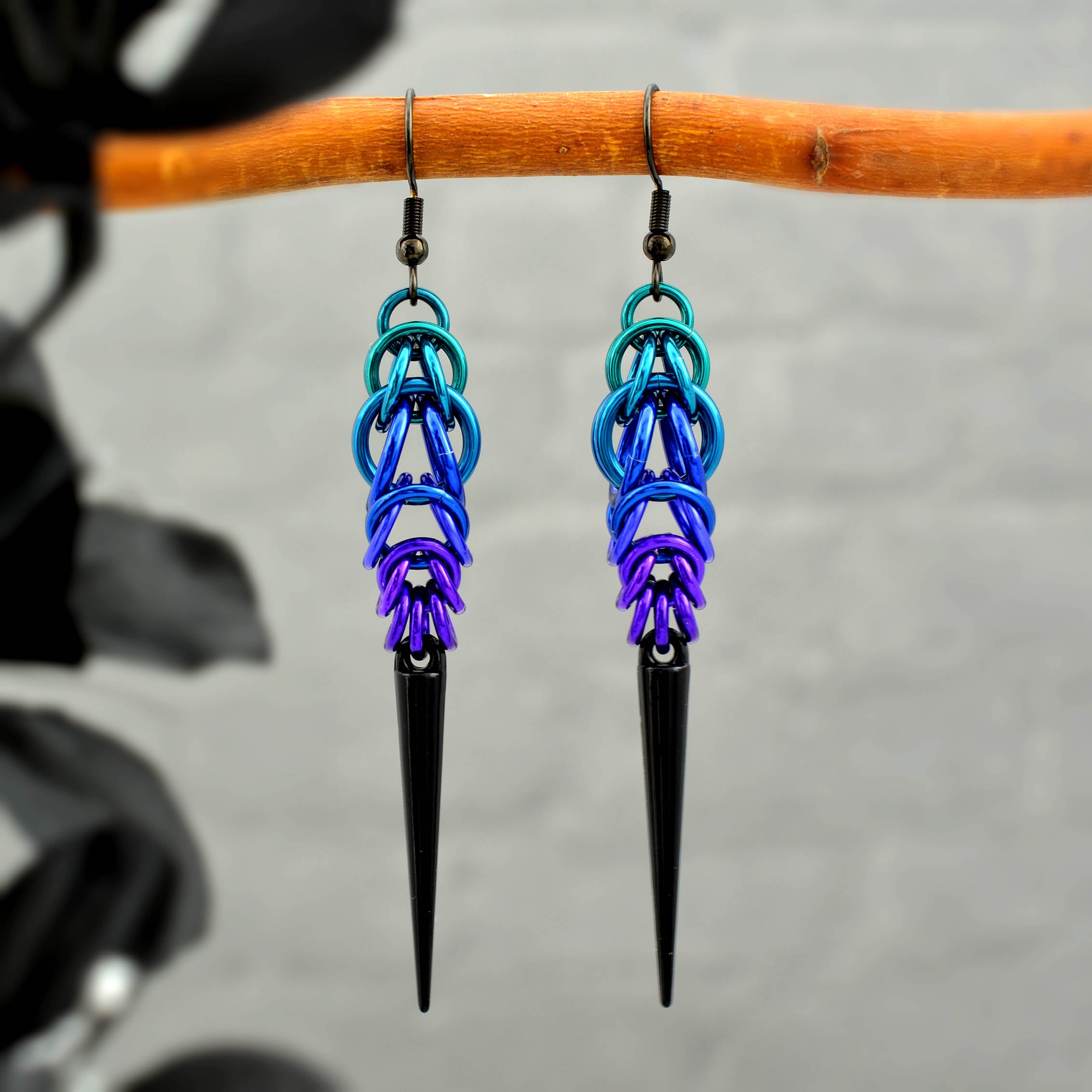 A pair of edgy chainmaile drop earrings with a black spike accent, featuring the Dark Mermaid ombre colors, hanging from a wooden branch.