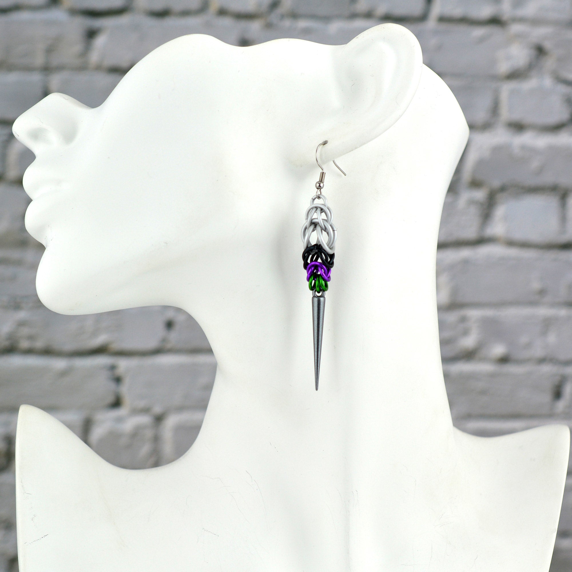 A Double Demi Pride spike earring displayed on a white mannequin head in profile. The earring features white, black, violet, and green chainmaille leading down to the dark grey acrylic spike.