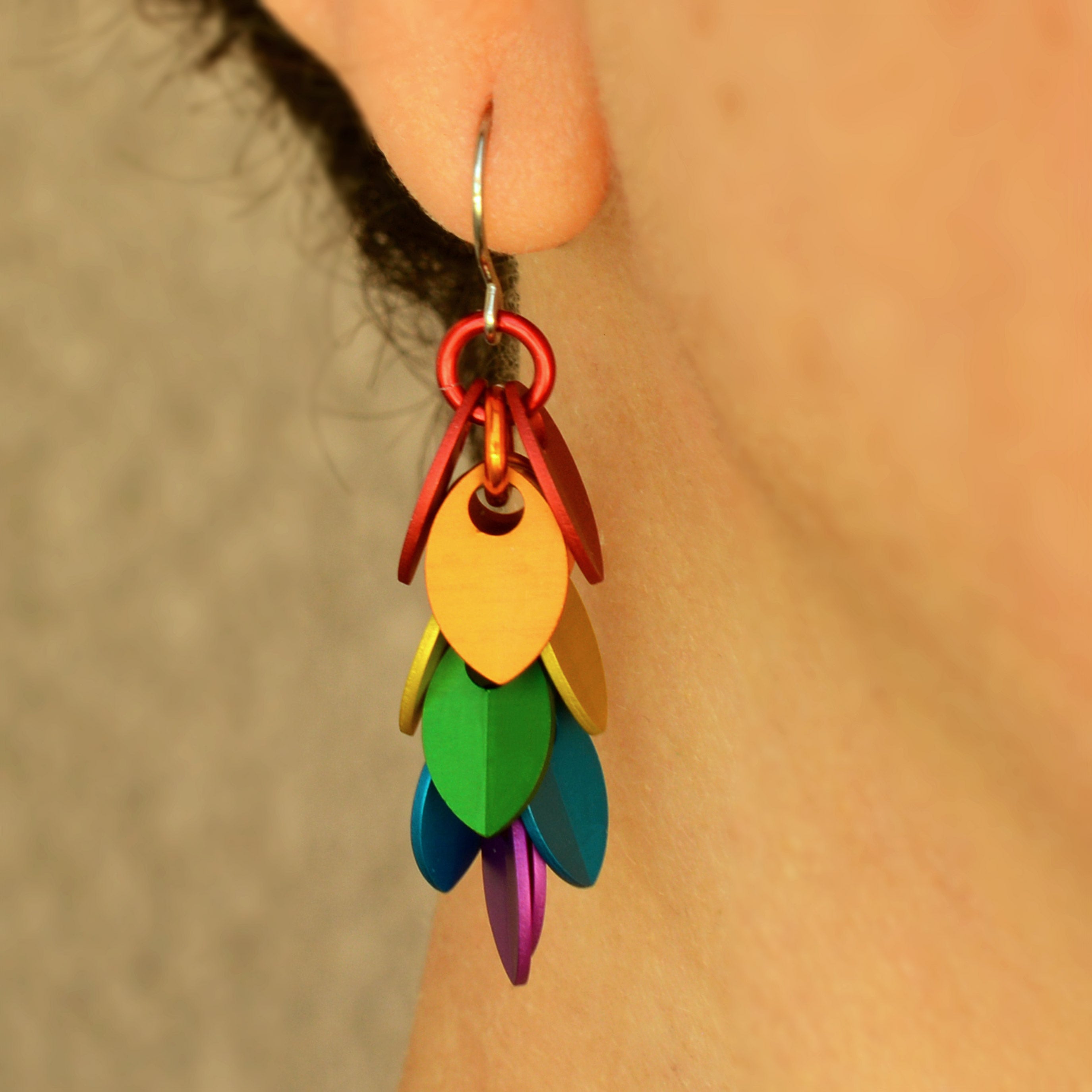Close-up of a mini Leaf Pride Dangle Earring by Rebeca Mojica Jewelry being worn on an ear. The colorful aluminum leaves are clearly visible.