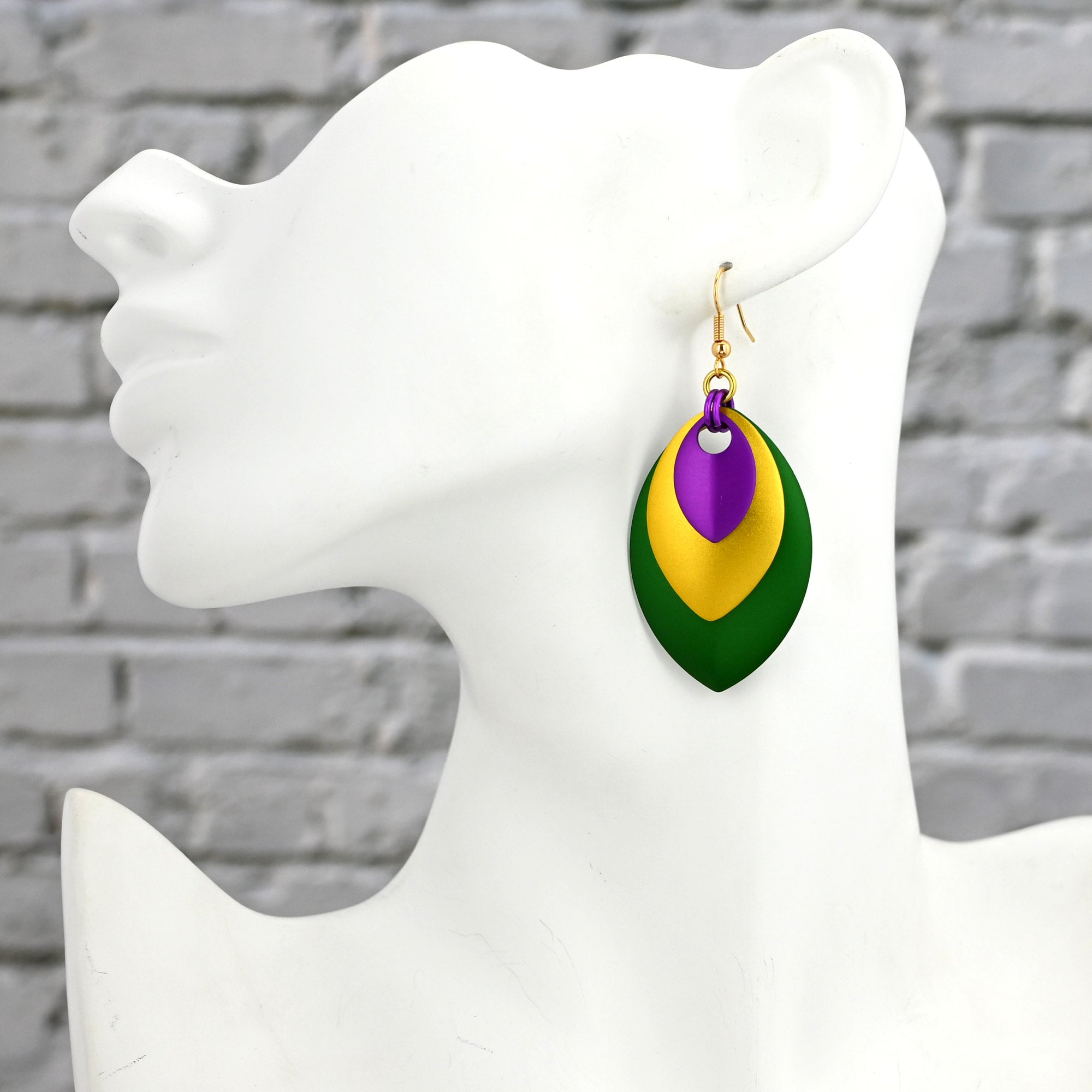 Side view of a white mannequin bust wearing a large stacked leaf earring to show how the bold purple, gold, and green design hangs.