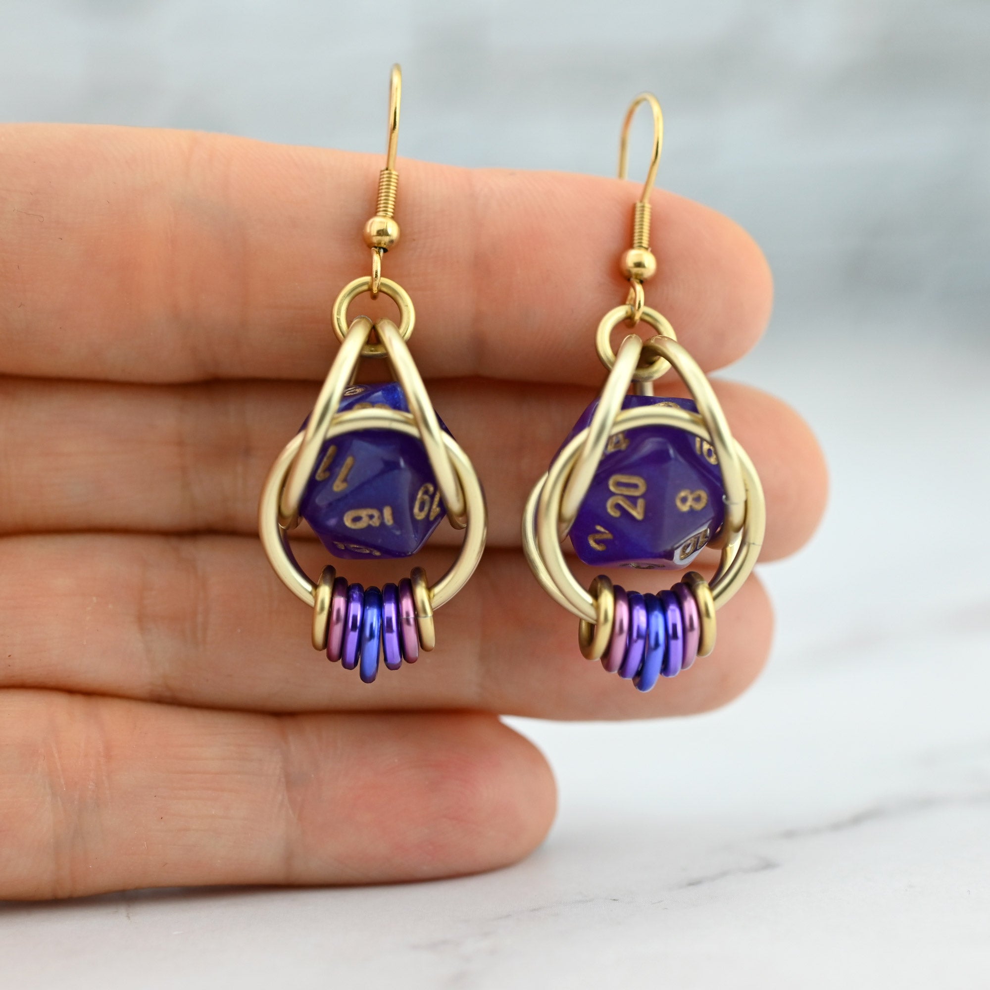 A person holding the Wisteria Fae d20 earrings to demonstrate the small size of the mini dice showcase the pastel vaporware color coil at the base.