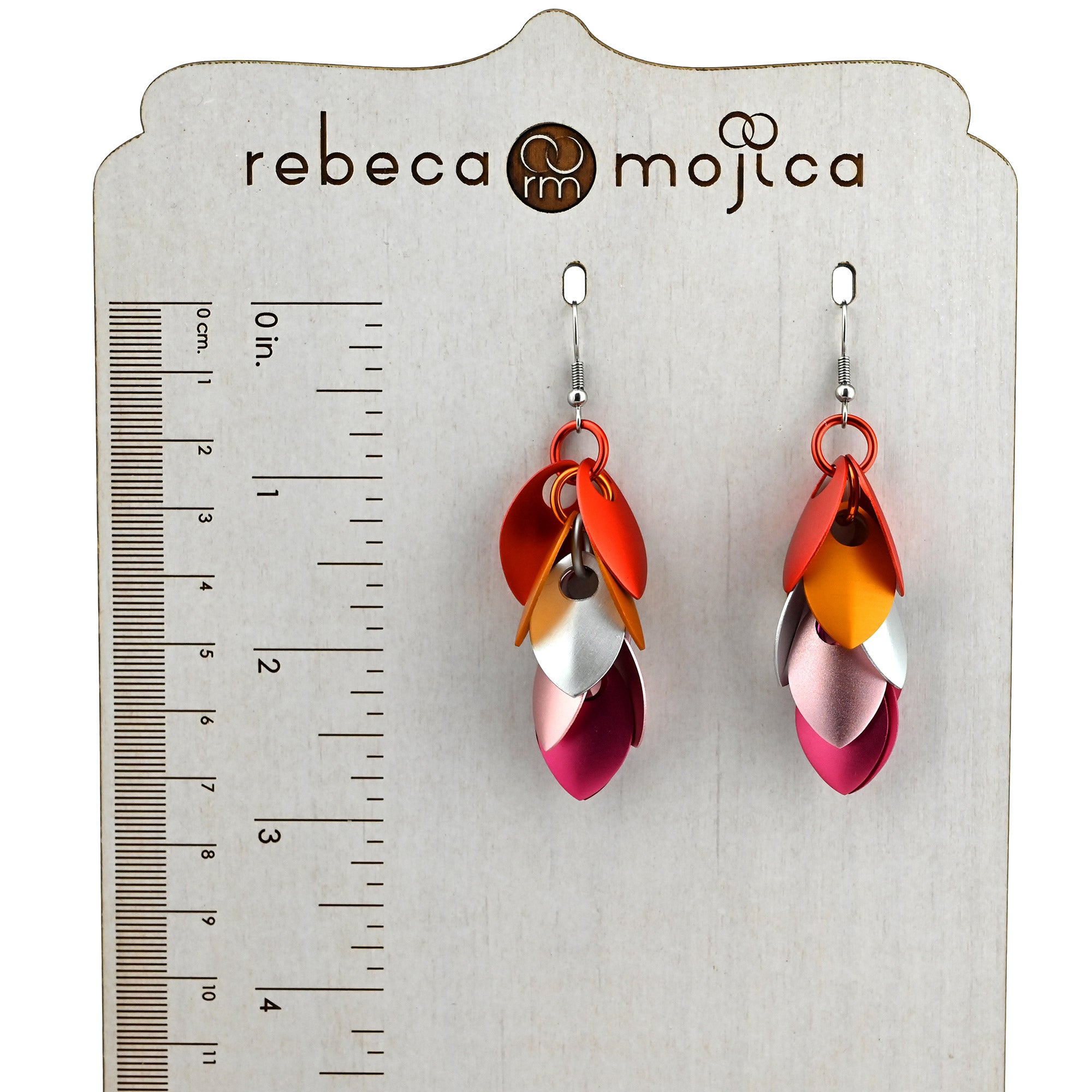The Lesbian Pride Cascading Leaves earrings shown on a Rebeca Mojica branded display card next to a ruler, measuring just under 3 inches in length.