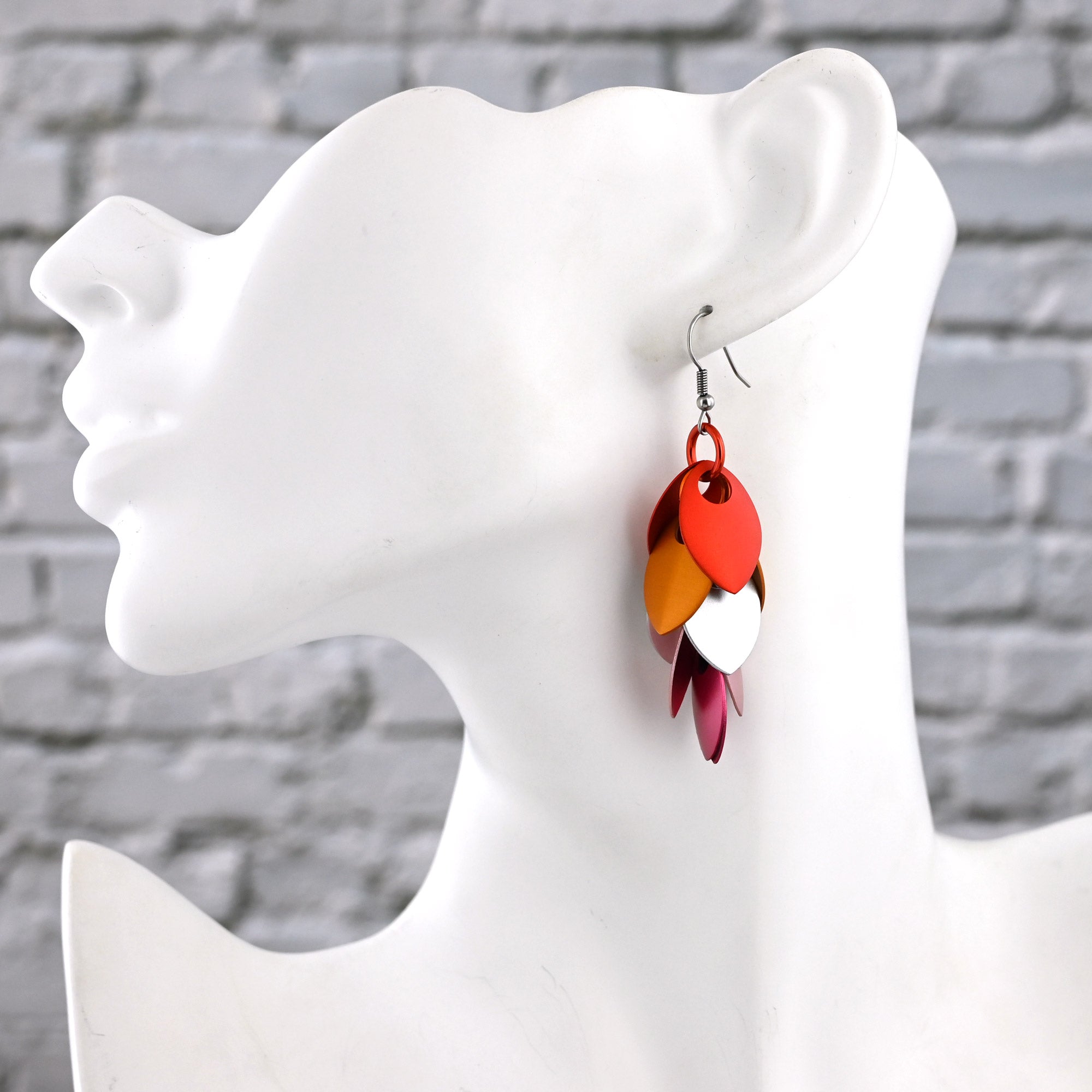 An alternate view of the side profile of a white mannequin bust wearing a long, feathered Lesbian Pride earring, showing how the 3-inch length sits against the neck.