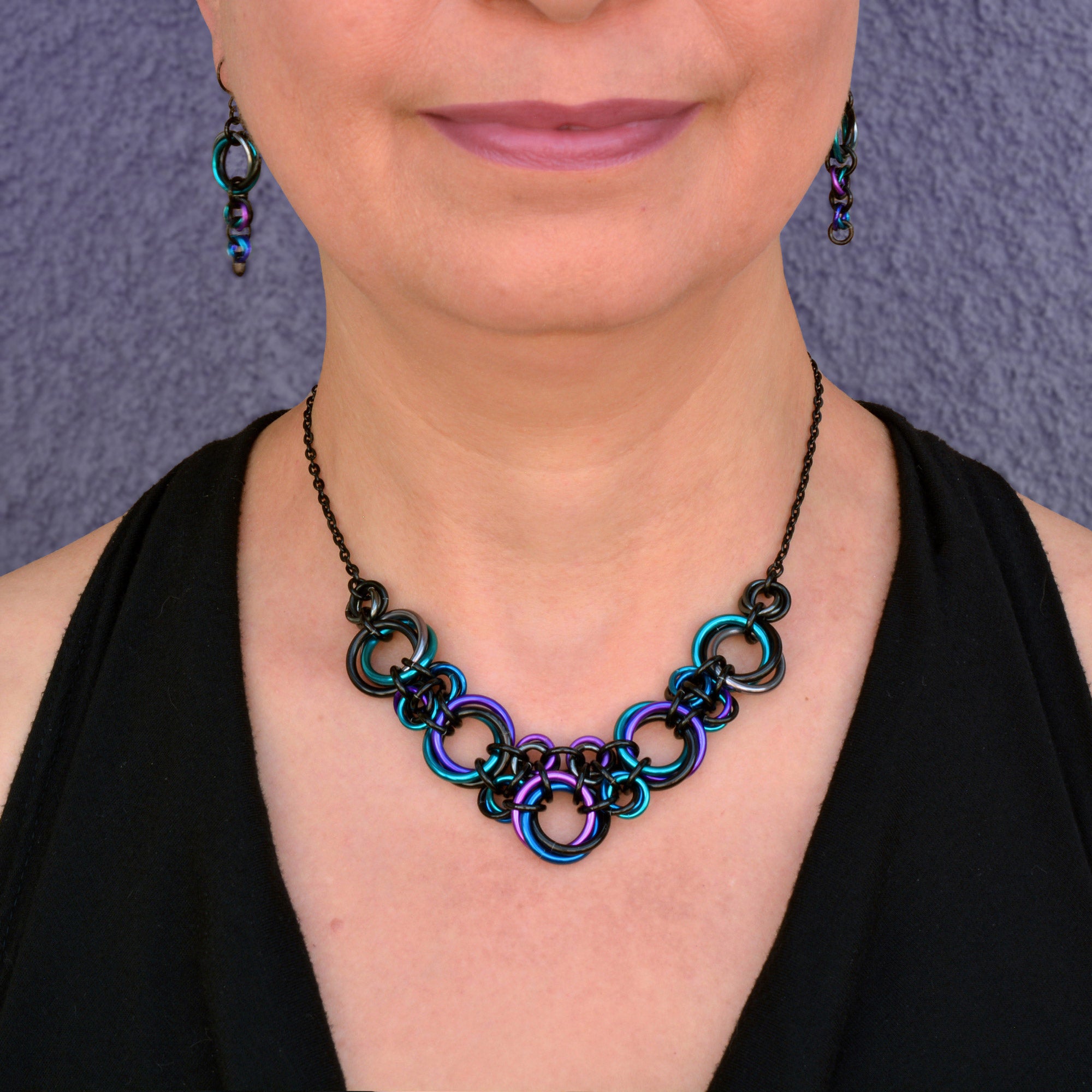 Close-up of Rebeca Mojica wearing the lightweight Knotted Metal V chainmail necklace and Comet earrings in Dark Mermaid (black, teal, purple, blue, violet).