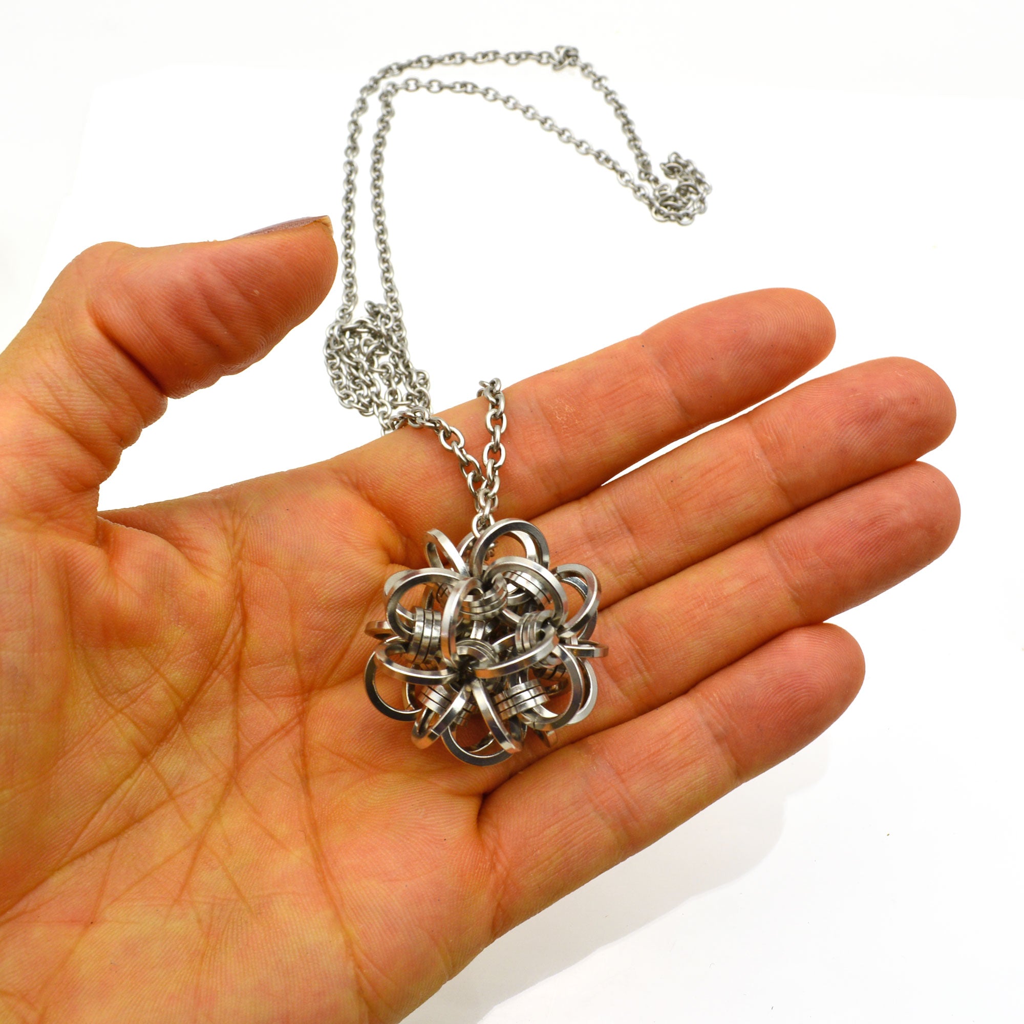 The dodecahedron chainmaille pendant (sphere) rests in the open palm of a hand, showing the complex, intricate texture of the steel pendant.