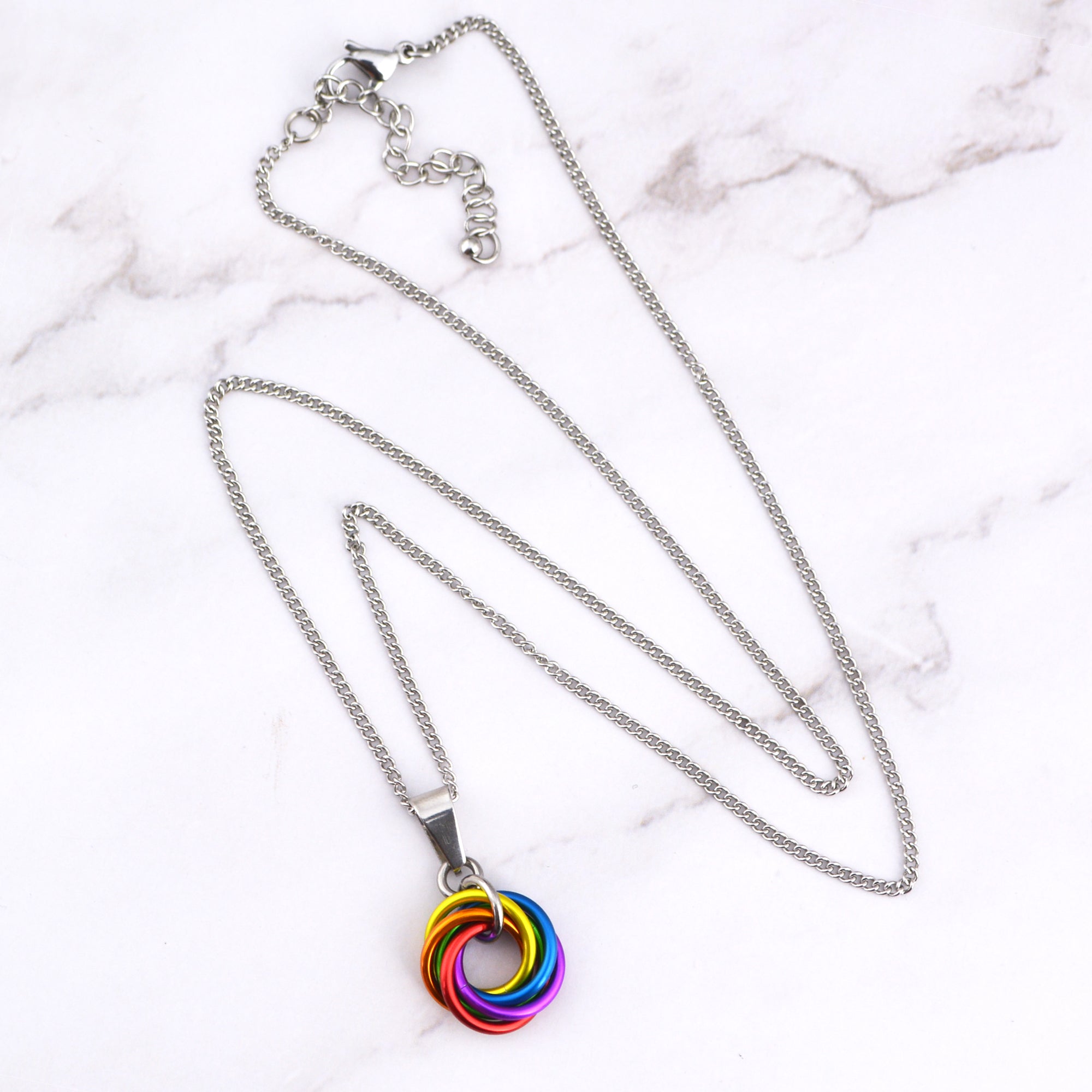 Stainless Steel chainnecklace with a small rainbow swirl pendant displayed on a white marble surface. The chain has an extender.