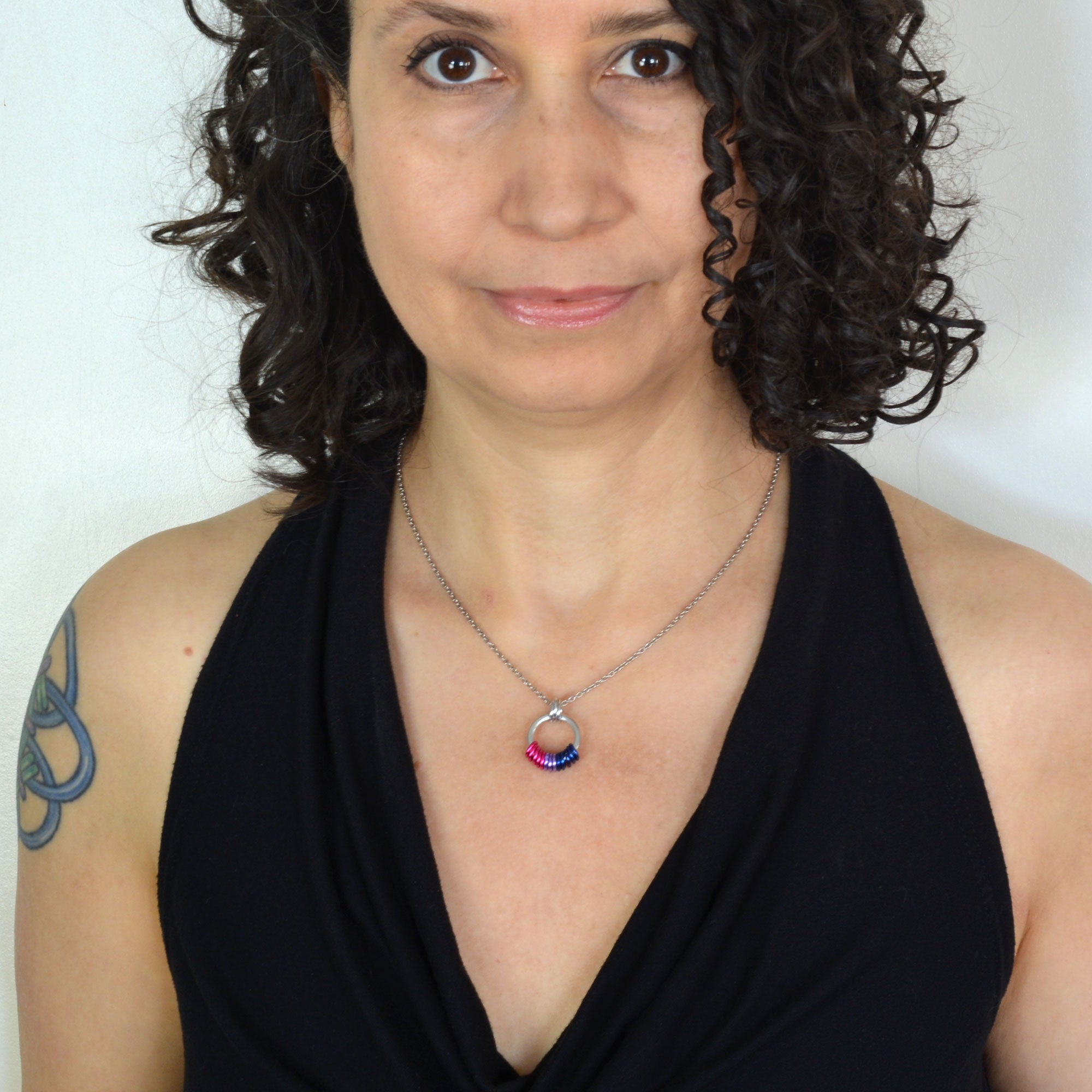 Woman with curly brown hair wearing a minimalist bi pride necklace and a black halter top.