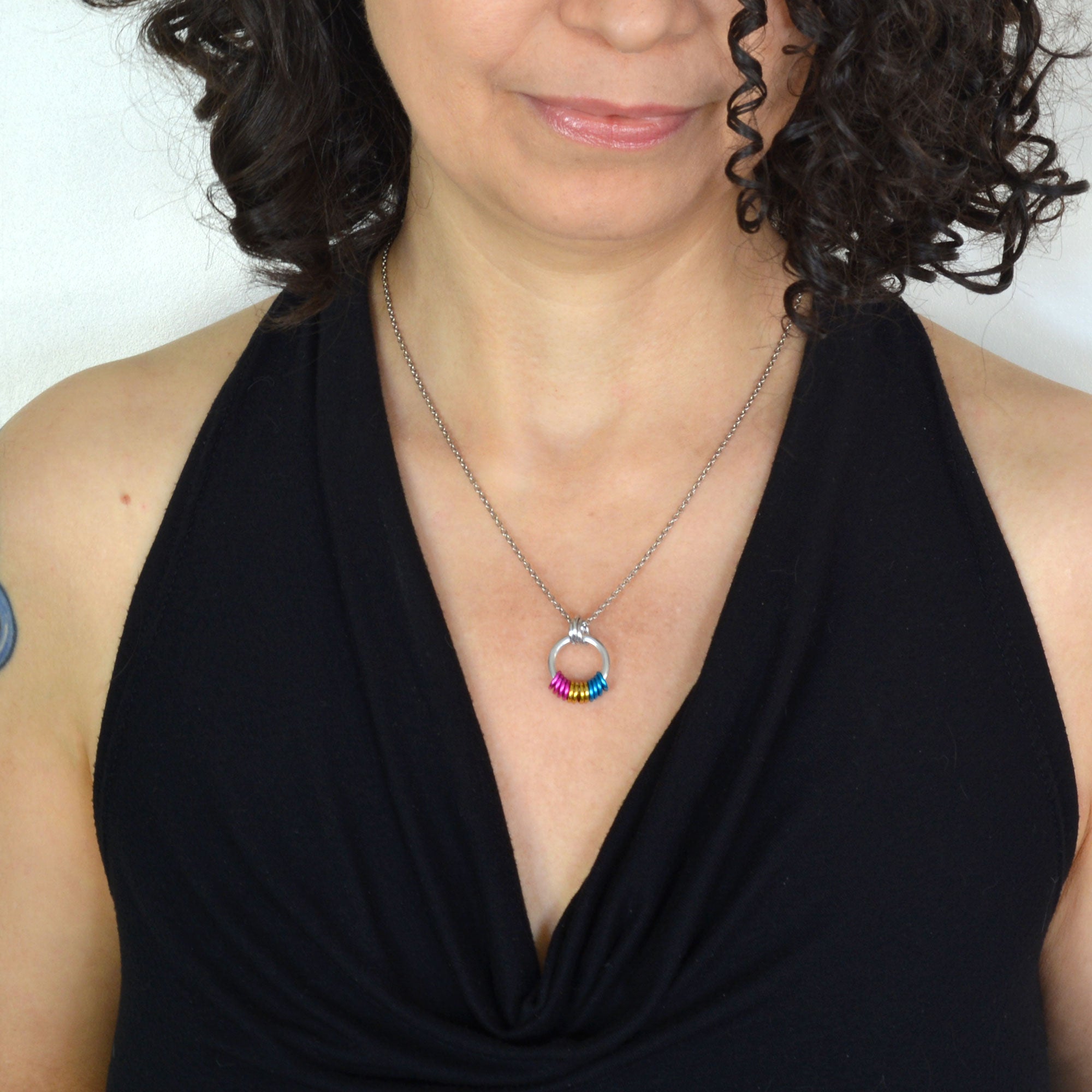 Woman with curly brown hair wearing a minimalist pan pride necklace and a black halter top.