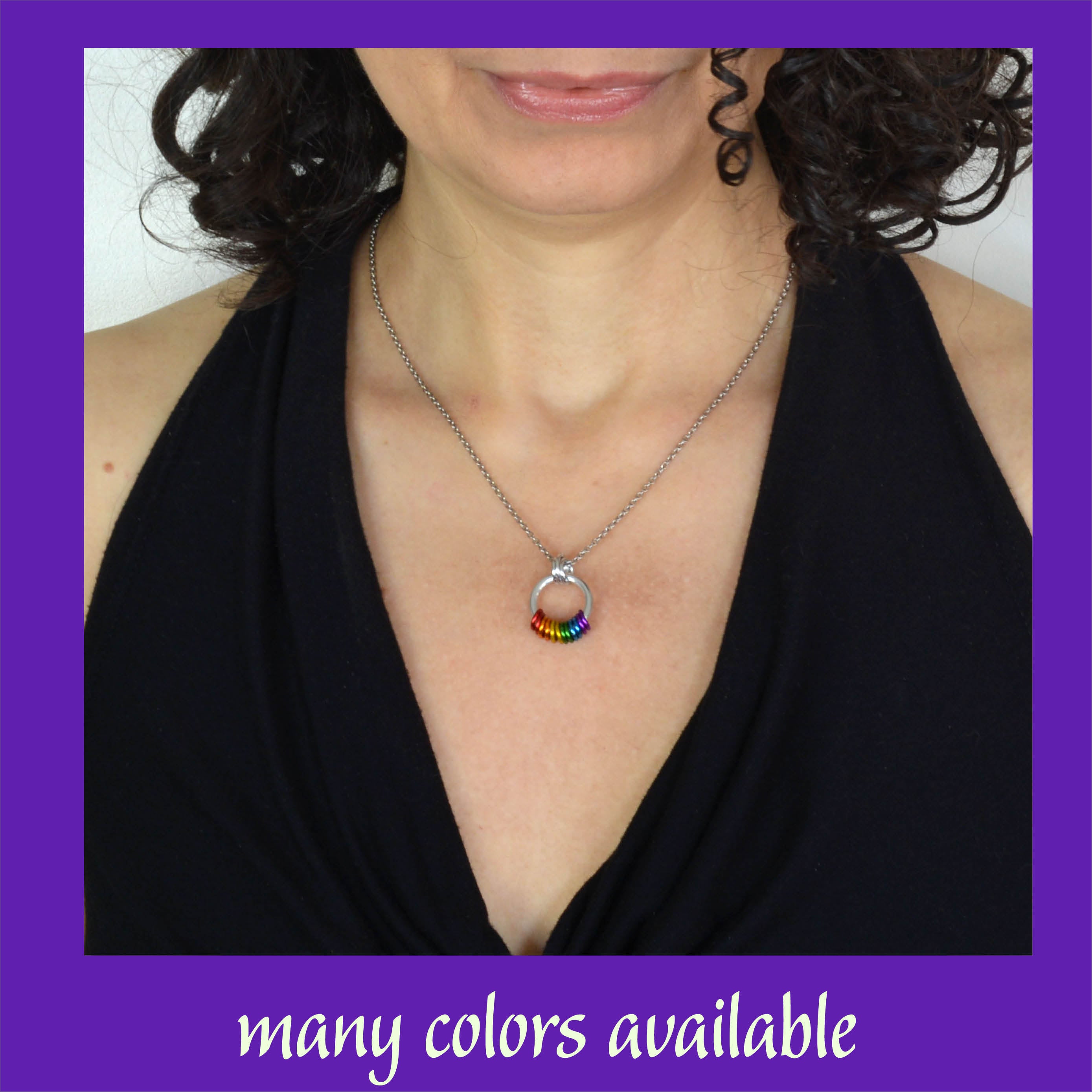 A close-up lifestyle shot of a person wearing the rainbow coil necklace against a black top. The pendant sits gracefully at the center of the chest, showcasing its dainty, minimalist appearance. The image is framed by a purple border with text at the bottom that reads “many colors available"