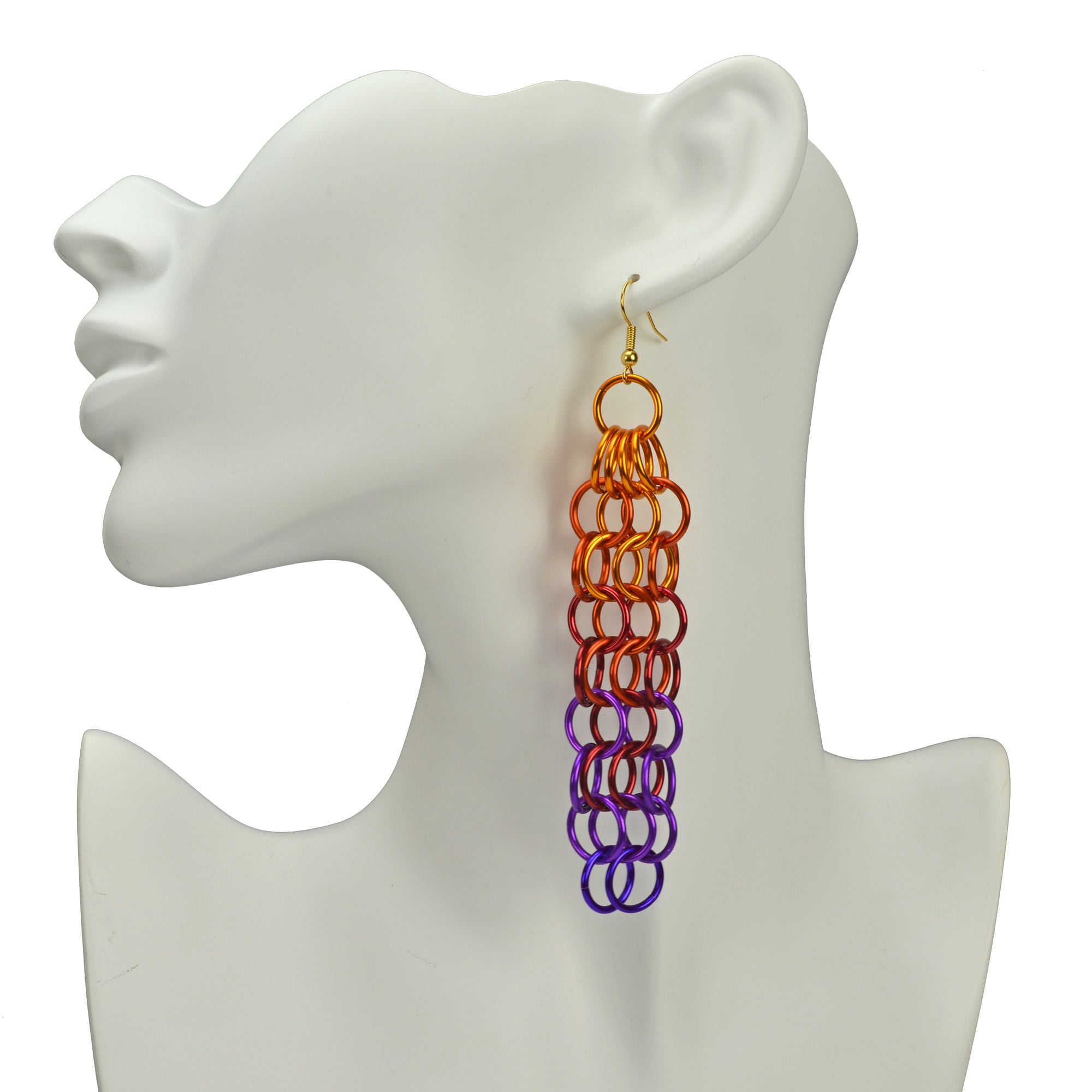 Long sunset ombre chainmaille earring hanging from the ear of a white display head. The earrings are a mesh pattern with orange at the top, transitioning to red, violet and purple.