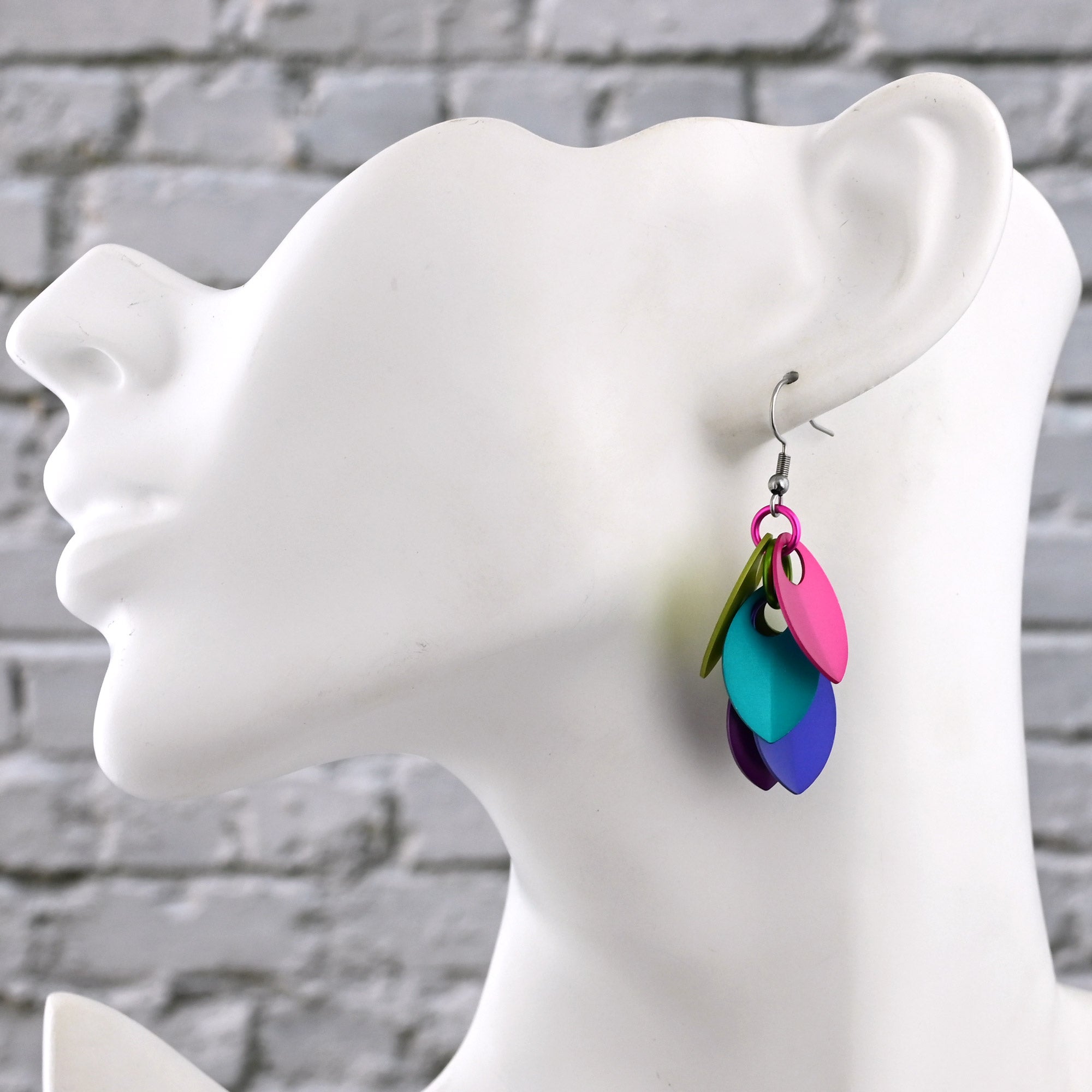Colorful earrings on a mannequin against a gray brick wall