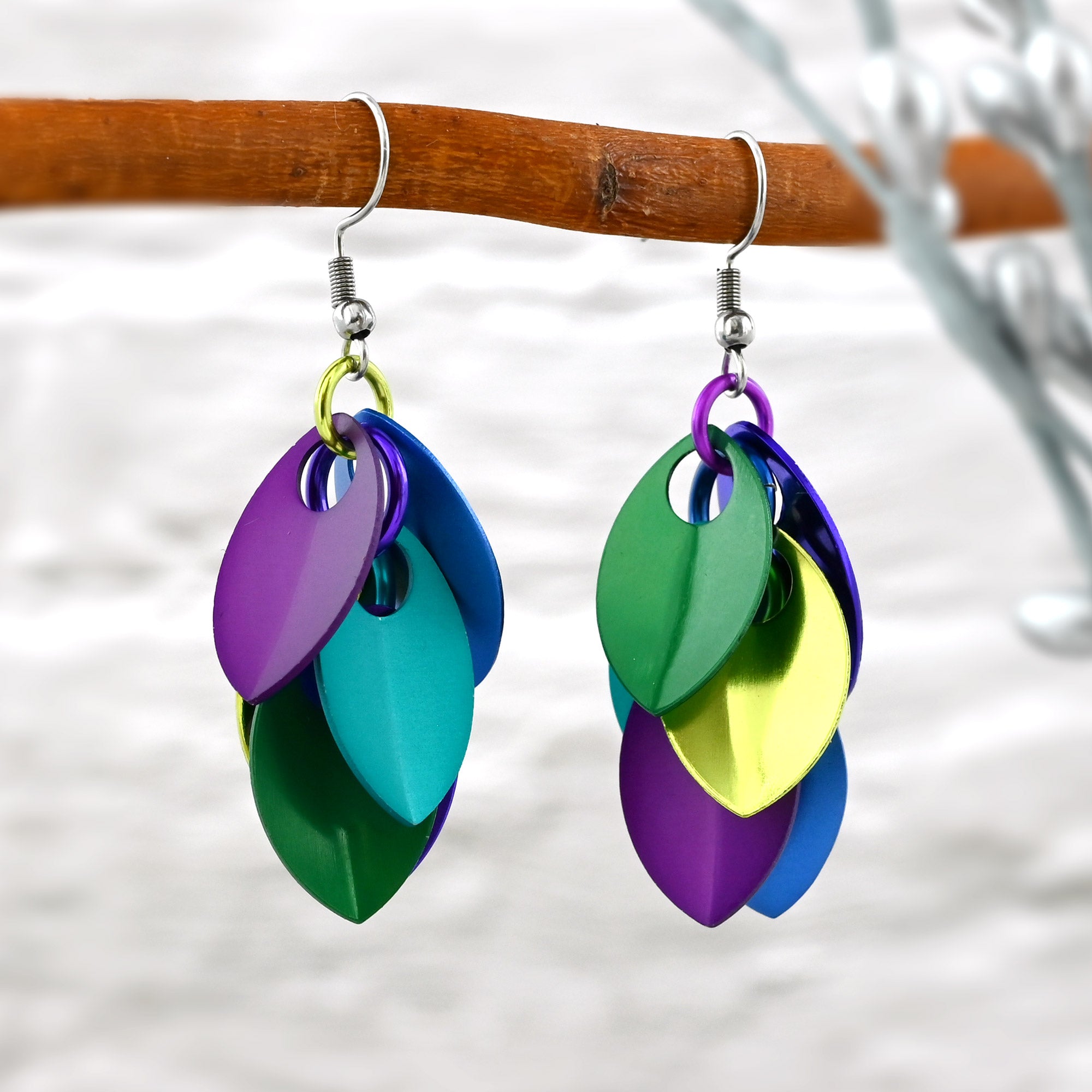 Close-up of the vibrant, multi-finish aluminum scales hanging from a wooden branch, highlighting the peacock color mix.