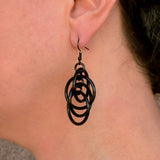 Close-up photo of Rebeca Mojica wearing one of the black intertwined hoop chainmaille earrings, showing the detail and how it dangles

