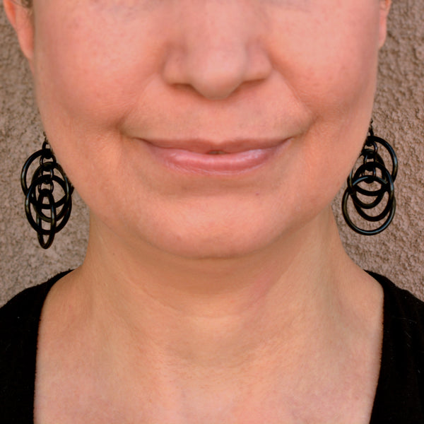 Rebeca Mojica wearing the black intertwined hoop chainmaille earrings, providing scale and how the earrings look.