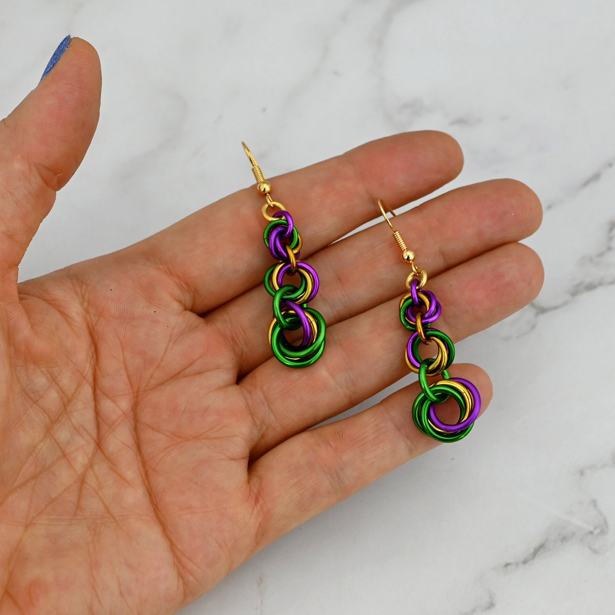 A pair of Mardi Gras graduated knot earrings resting in a palm to demonstrate their small, lightweight scale.