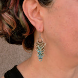 Artisan Rebeca Mojica wears a single seashell color teardrop mesh earring. The earring hangs just below her earlobe, showing its length and how it looks when worn. She has short, dark hair.