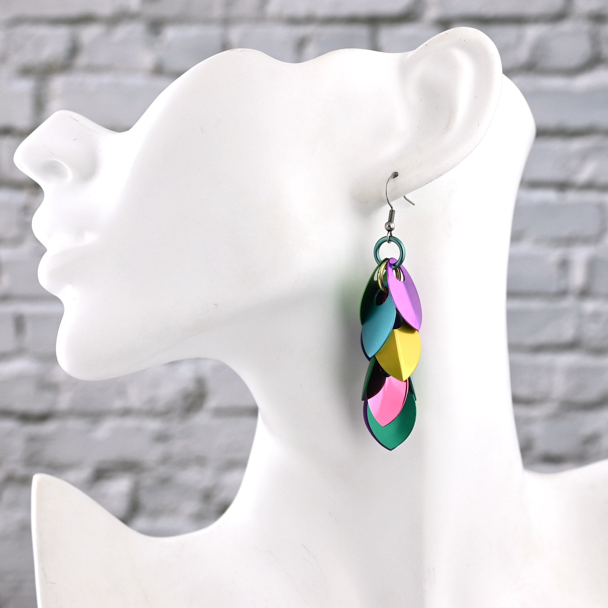Side view of a white mannequin wearing a long scalemaille earring in a variety of pastel colors, showing the 3-inch drop reaching mid-neck.