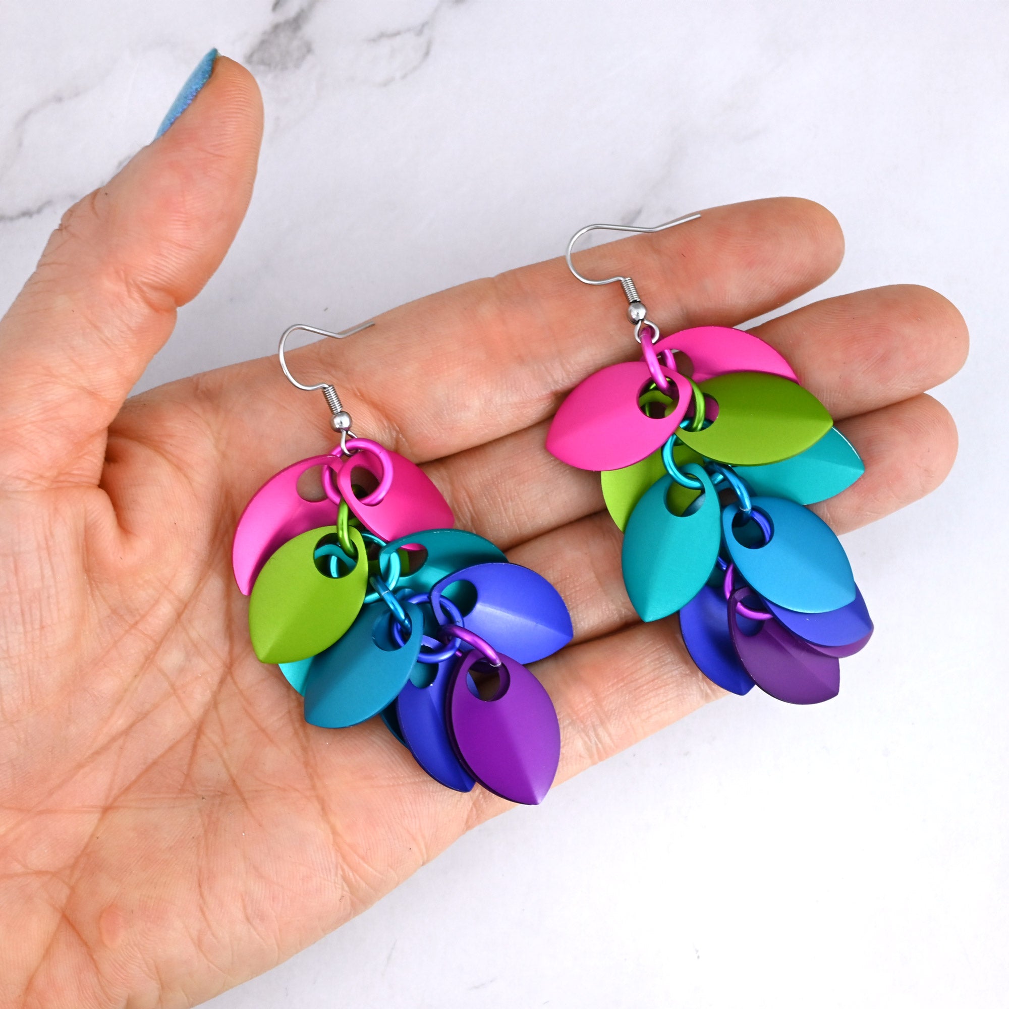 A person holding the long rainbow scale earrings to demonstrate their dramatic length and vibrant colors.