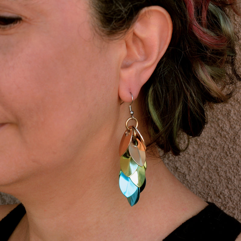 An angled, close-up shot of the earring being worn on artisan Rebeca Mojica's ear and showcasing the reflective nature of the scalemaille components.
