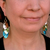 A photo of artisan Rebeca Mojica wearing the long, elegant scalemaille earrings in champagne, seafoam and blue colors, showcasing how the “leaves” (scales” reflect the light

