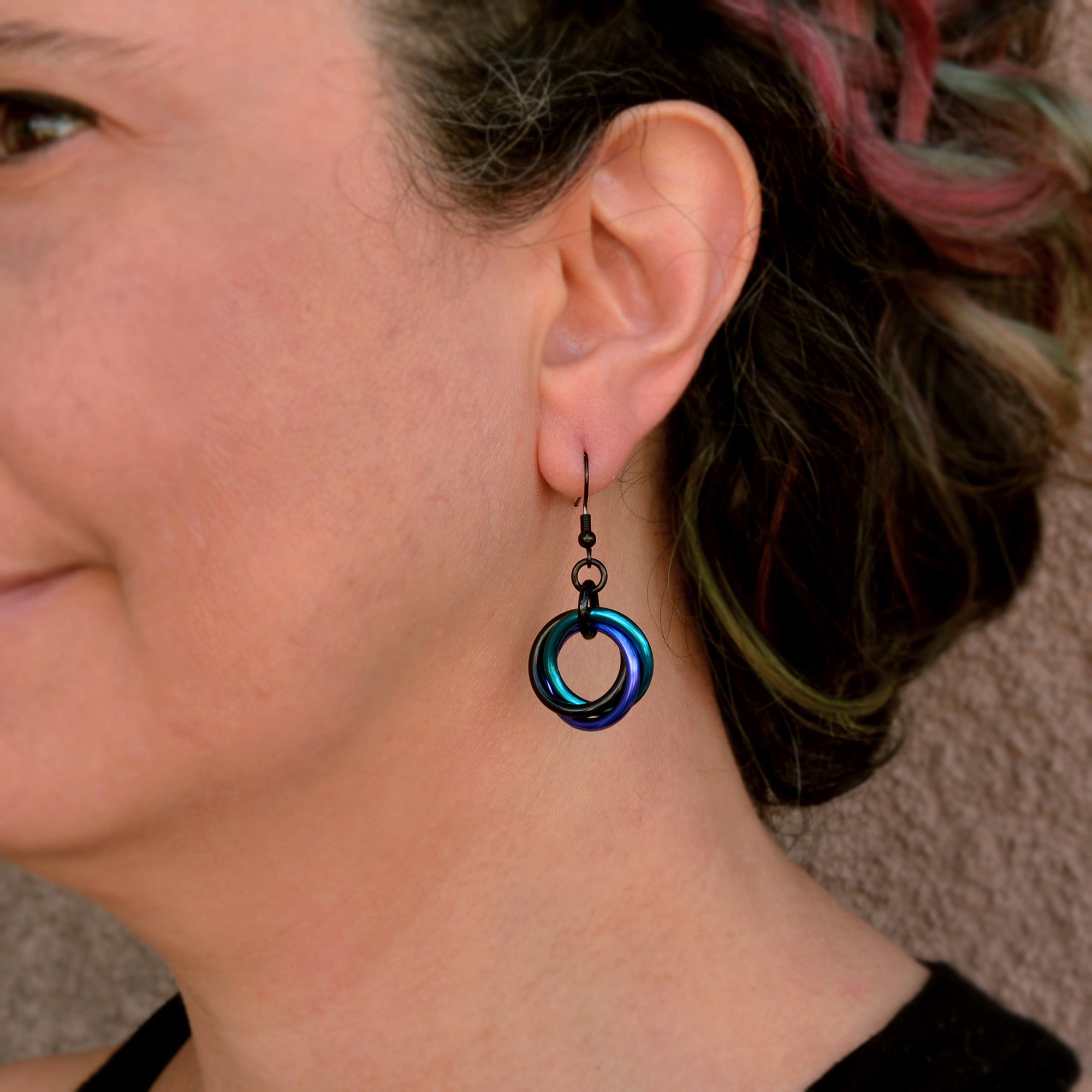 Lightweight Single Knot earrings in Dark Mermaid (purple, teal, black) modeled by artisan Rebeca Mojica for a scale and fit reference.