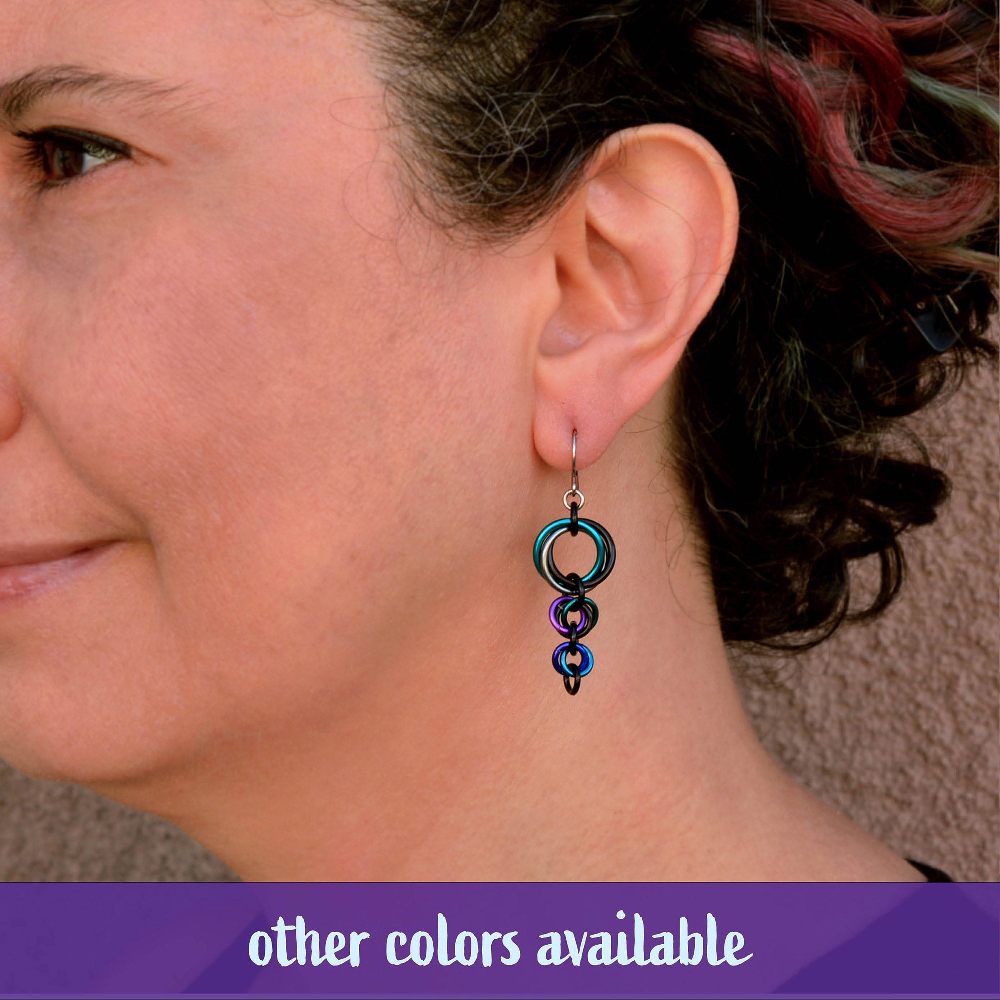 A person wearing a similar triple-knot earring style in a teal and blue ombre to demonstrate the scale of the Comet Earring when worn, and show how it hangs.
