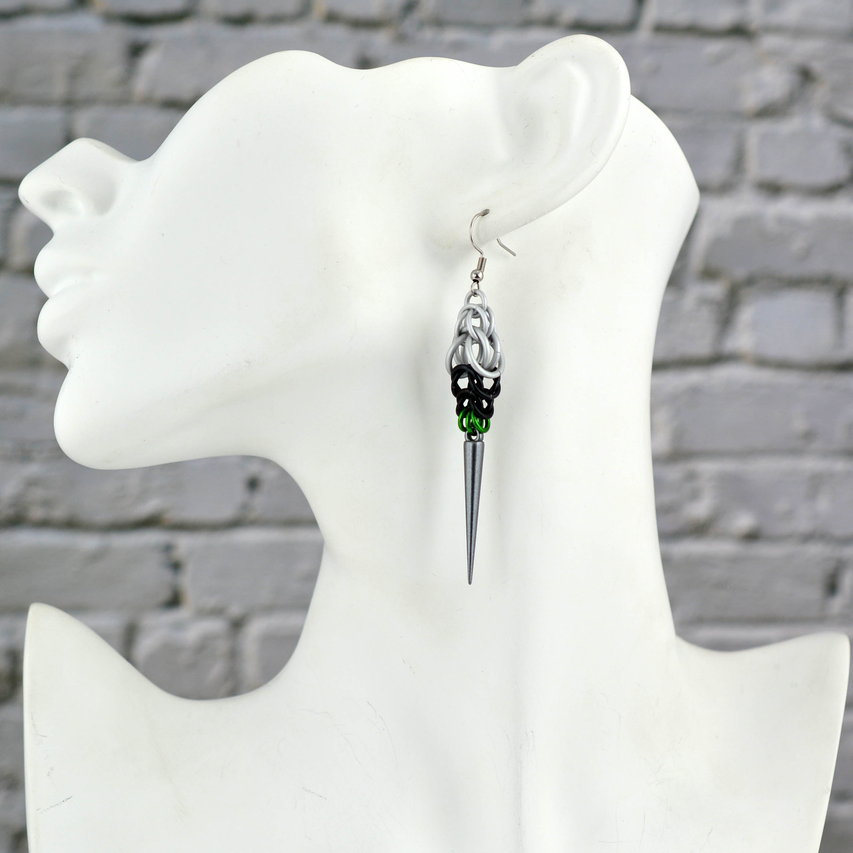 A Demiromantic Pride spike earring displayed on a white mannequin head in profile. The earring features white, black, and green chainmaille leading down to the dark grey acrylic spike.