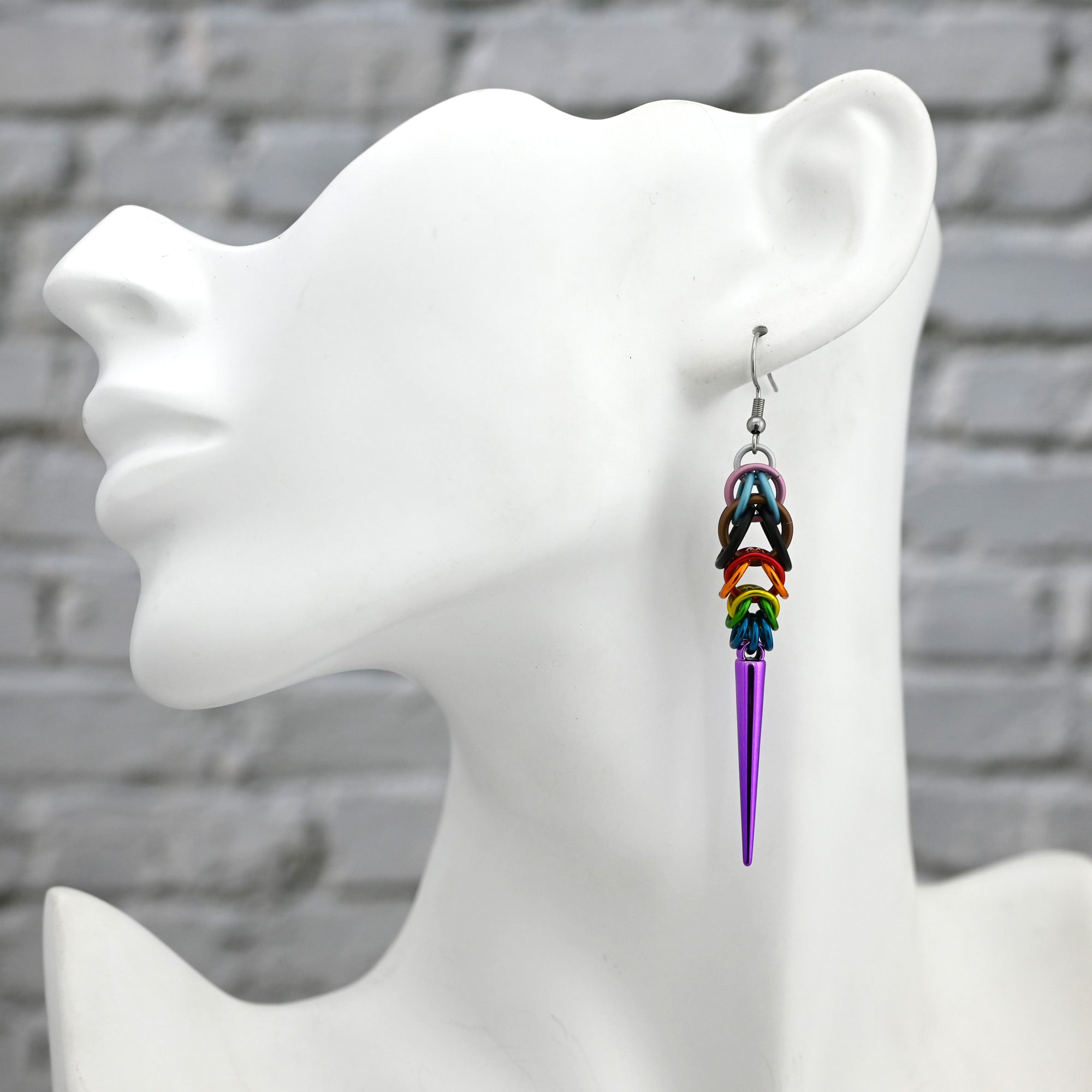A single Progress Pride spike earring worn on a white mannequin head to show the 3.25-inch length and how the chainmaille drapes against the neck.