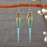 Handmade Seashell Ombre Chainmaille Spike Earrings hanging from a branch, with a soft-focus background of nature to emphasize their boho-edgy style. Earrings are a gradient of beige, seafoam and light blue chainmail links with a light blue spike at the base