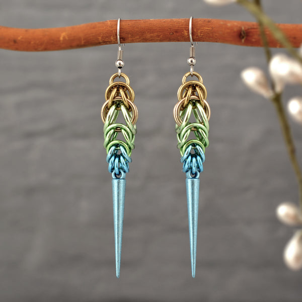 Handmade Seashell Ombre Chainmaille Spike Earrings hanging from a branch, with a soft-focus background of nature to emphasize their boho-edgy style. Earrings are a gradient of beige, seafoam and light blue chainmail links with a light blue spike at the base