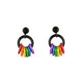 A clean, white background showcases two rainbow pride earrings with black stud posts and black rings. Small rings dangle in the colors of the rainbow pride flag: red, orange, yellow, green, azure, and violet. The colors are mirrored on the earring on the right.