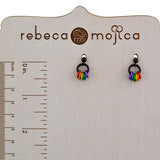 A pair of black post rainbow pride earrings displayed on a light wooden stand with a ruler measurement on the left side, showing dimensions in both centimeters and inches. These earrings measure about 0.5” from the top of the post to the bottom of the colorful links. The brand "rebeca mojica" is visible at the top.