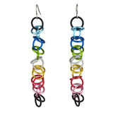 Two individual Queer Pride orbital earrings are presented against a clean white background. Each earring is made up of small, brightly colored aluminum rings linked in a chainmaille design, displaying the Queer Pride flag colors: black, light blue, blue, bright green, white, gold, dark pink, pink, and black. They each feature a simple steel fishhook earwire at the top, clearly showing the structure and color sequence.