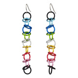 Against a stark white backdrop, two Queer Pride orbital earrings are displayed individually. Small, vibrant aluminum rings are linked in a chainmaille pattern to form each earring, showcasing the Queer Pride flag colors: black, light blue, blue, bright green, white, gold, dark pink, pink, and black. A simple steel fishhook earwire is attached to the top of each, clearly illustrating the earring's construction and color arrangement.