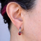 Side view closeup of a 12mm stainless steel huggie earring being worn in an earlobe. Because of the side view, only the red link of the lgbtq pride rainbow is visible; the other colors are stacked behind the red link