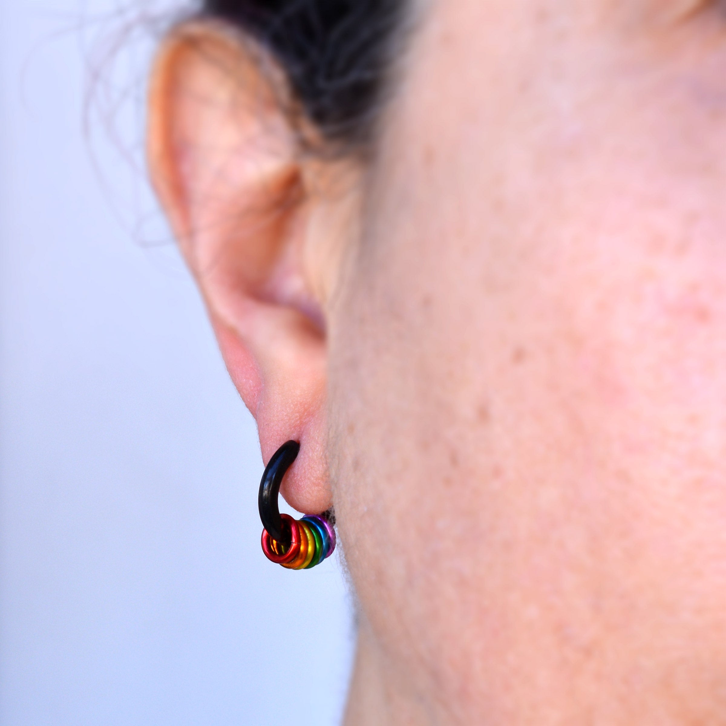Close-up of a rainbow pride huggie earring in black being worn in an earlobe